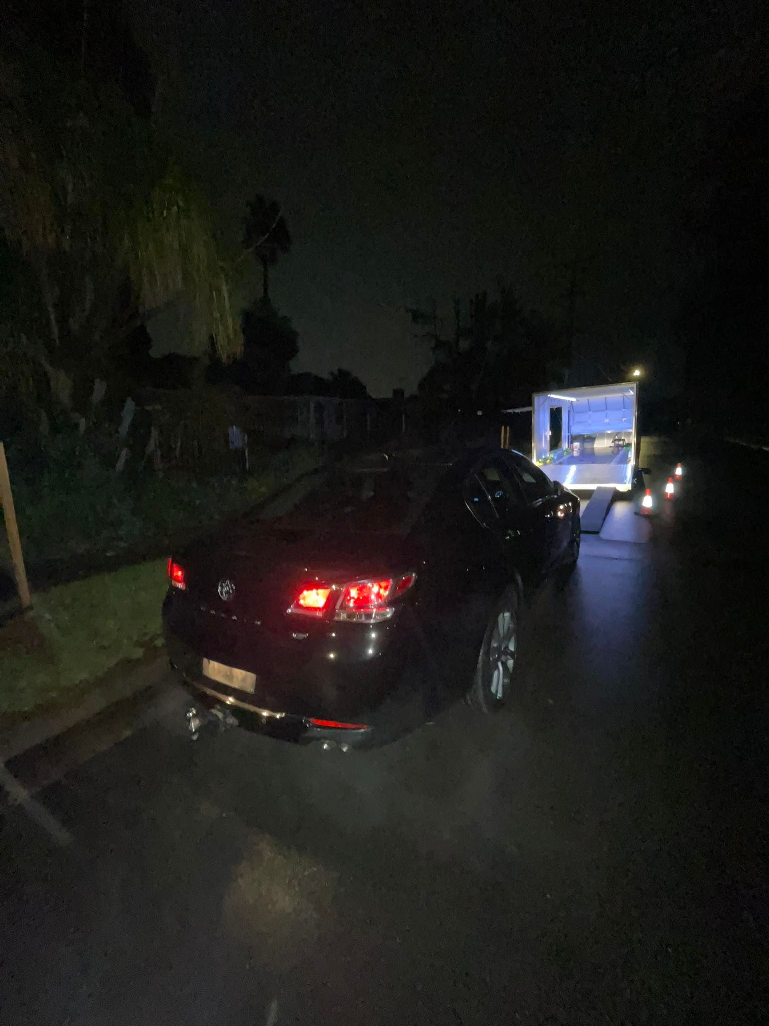Black car pulling a trailer on a dark street at night, with illuminated trailer — Full Throttle Enclosed Car Transport in Kilmore, VIC