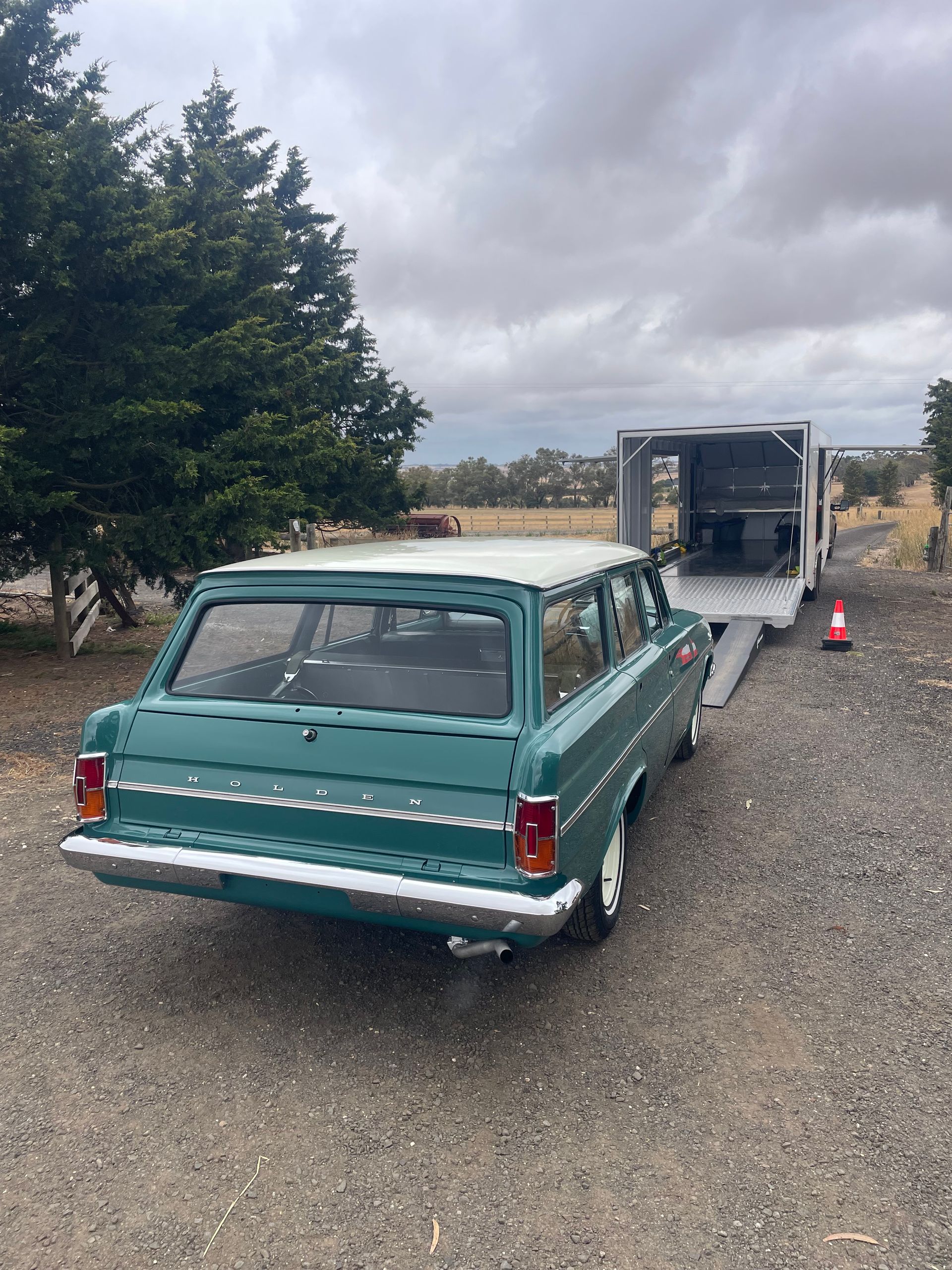 Teal vintage station wagon parked on gravel beside a trailer under cloudy skies. -Full Throttle Enclosed Car Transport in Kilmore, VIC