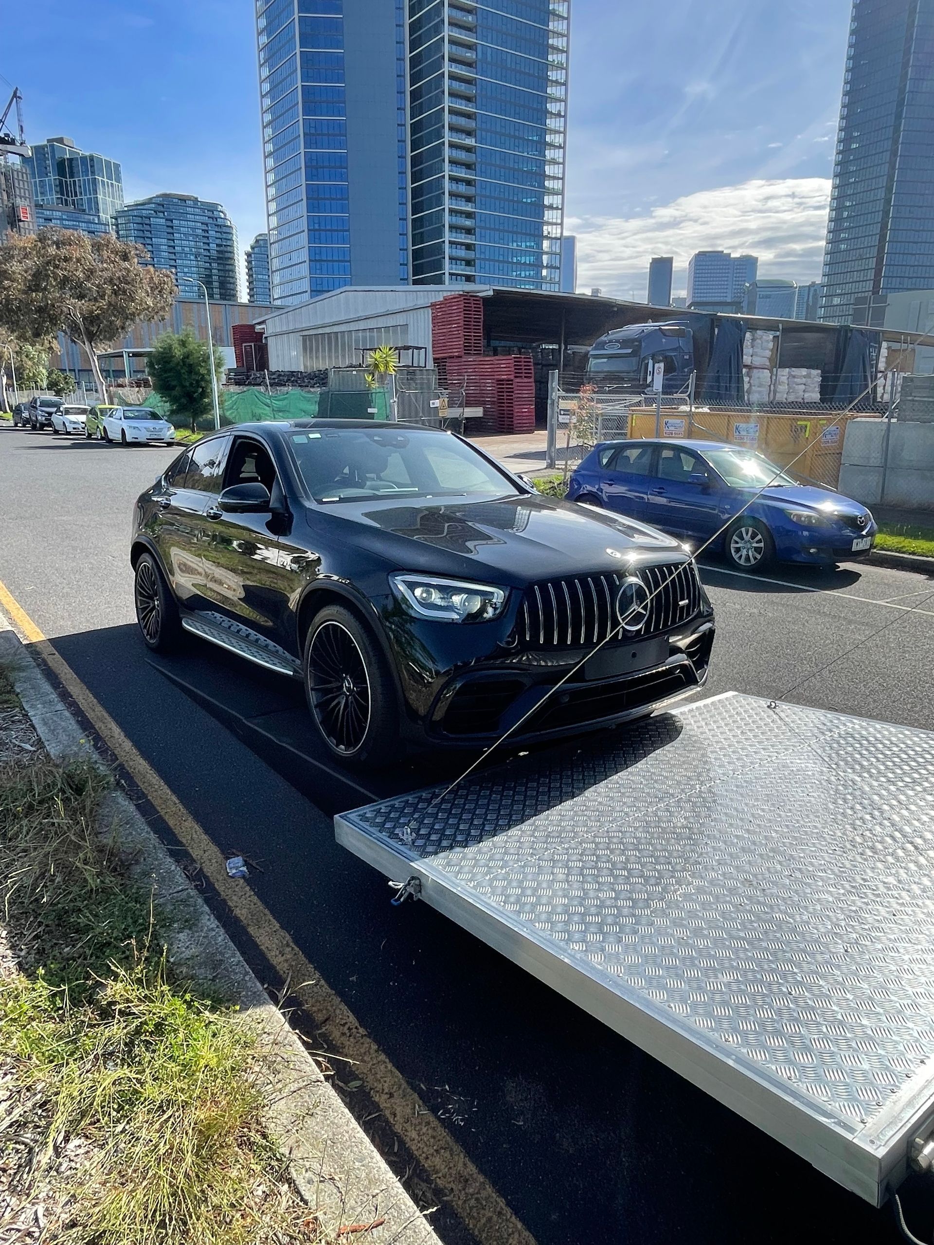 Black luxury SUV on a flatbed tow truck on a city street with high-rise buildings in the background - Full Throttle Enclosed Car Transport in Kilmore, VIC