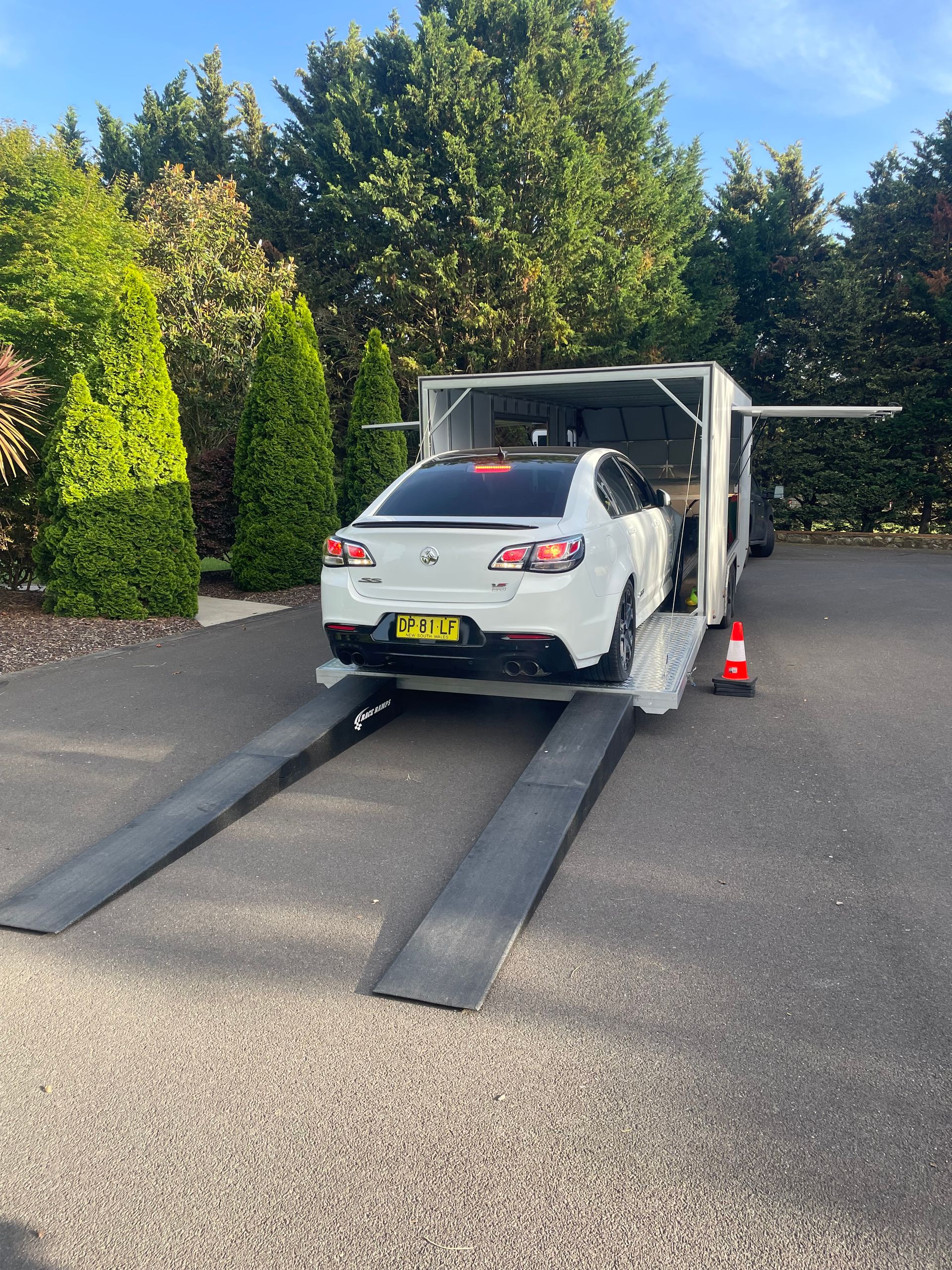 White car on a tow truck ramp in a driveway, with cones and trees nearby. - Full Throttle Enclosed Car Transport in Kilmore, VIC