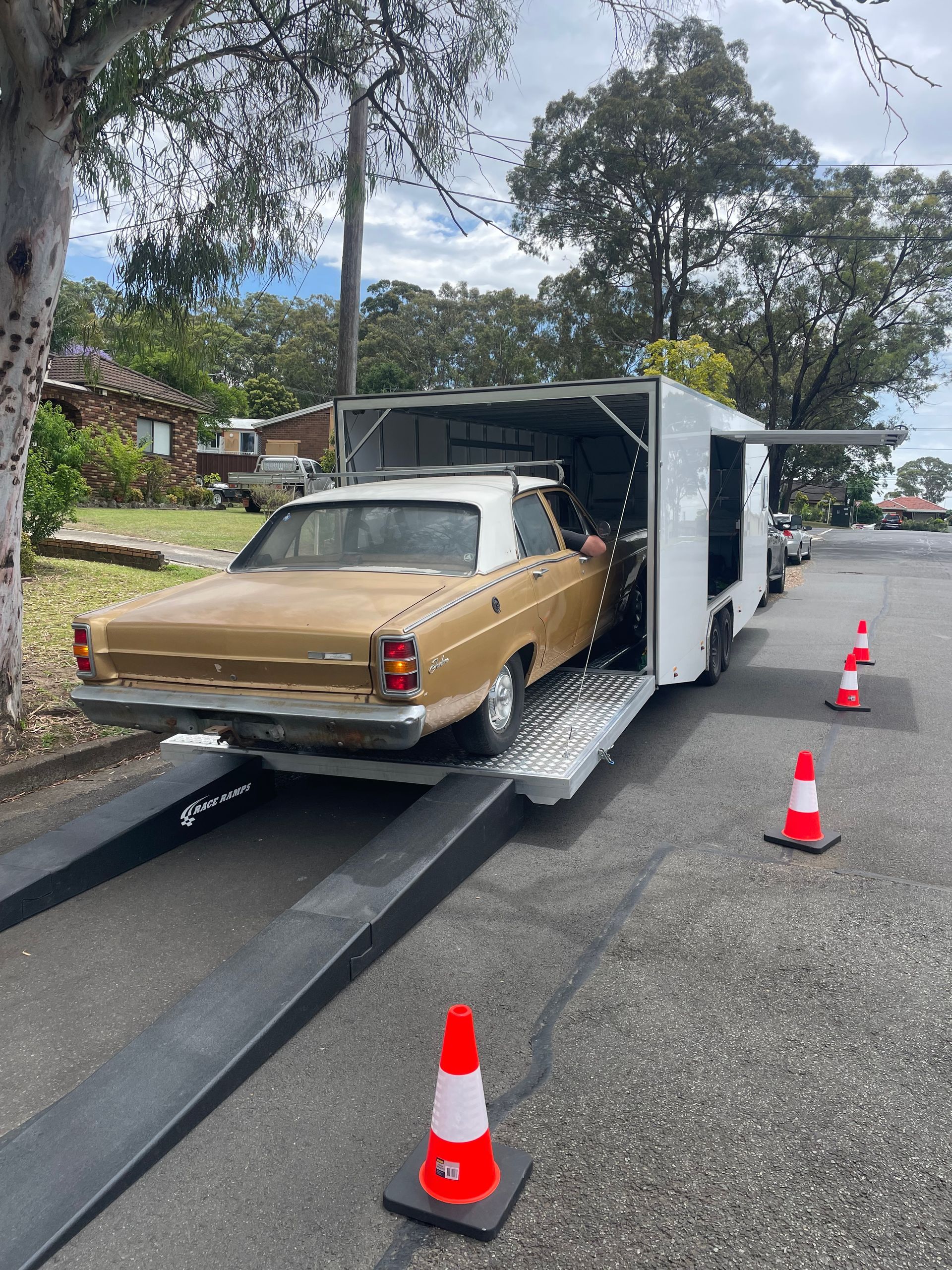 Tan sedan loaded on a car trailer, with orange cones on a residential street. - Full Throttle Enclosed Car Transport in Kilmore, VIC