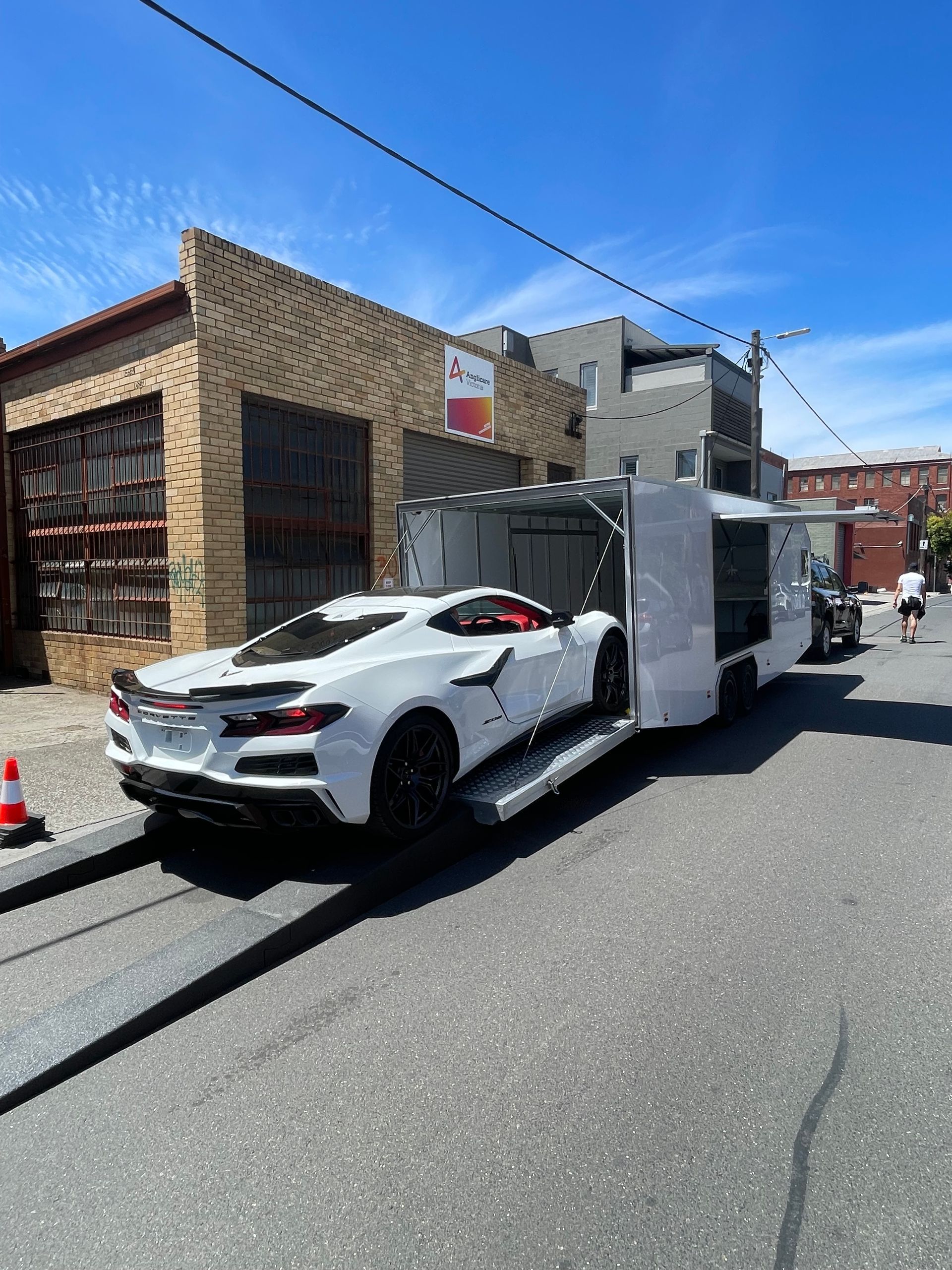 White sports car on a tow truck parked along a sunny city street with brick buildings. -Full Throttle Enclosed Car Transport in Kilmore, VIC