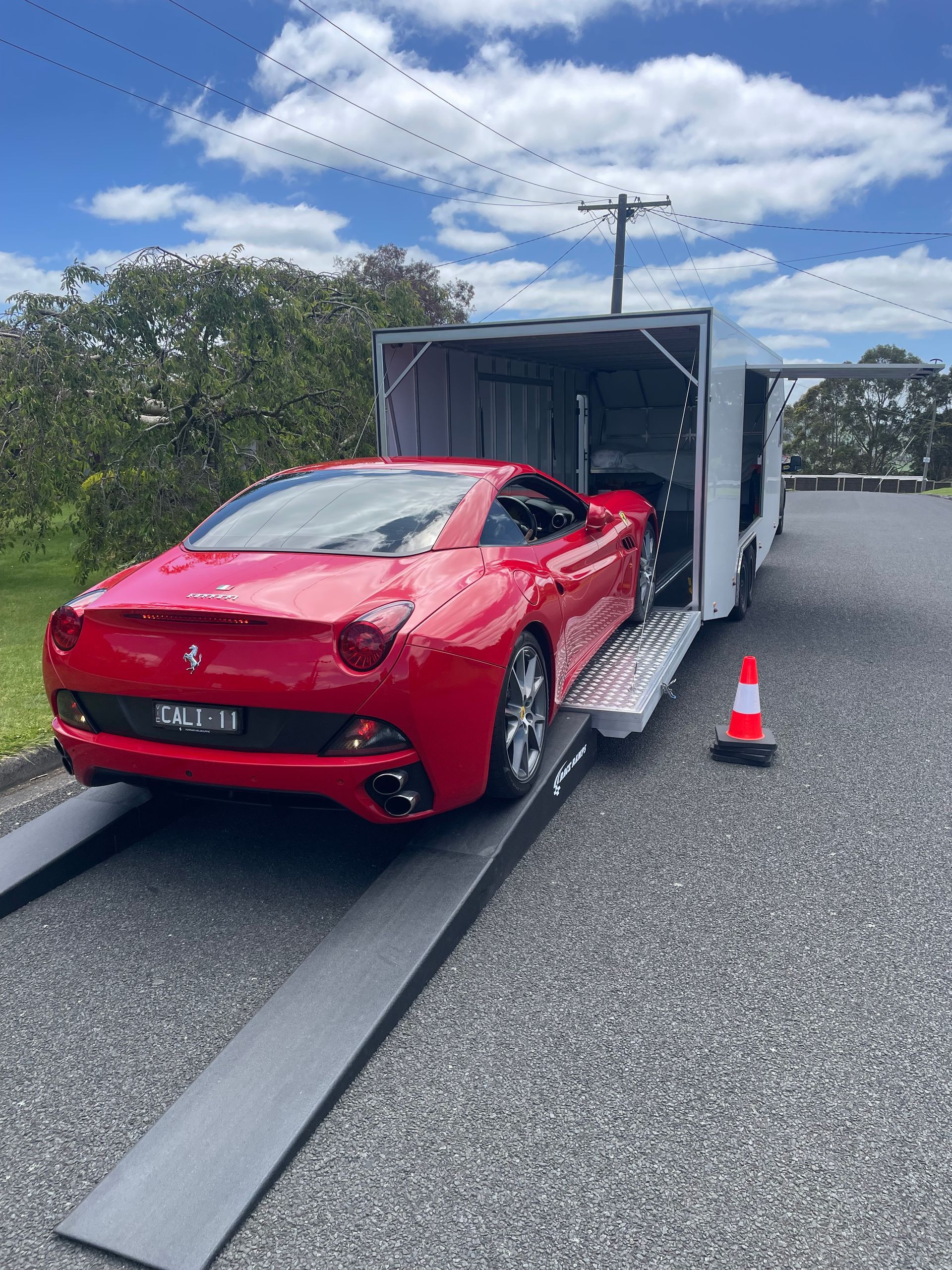 Red sports car loading onto a car carrier trailer on a roadside under a cloudy sky.
