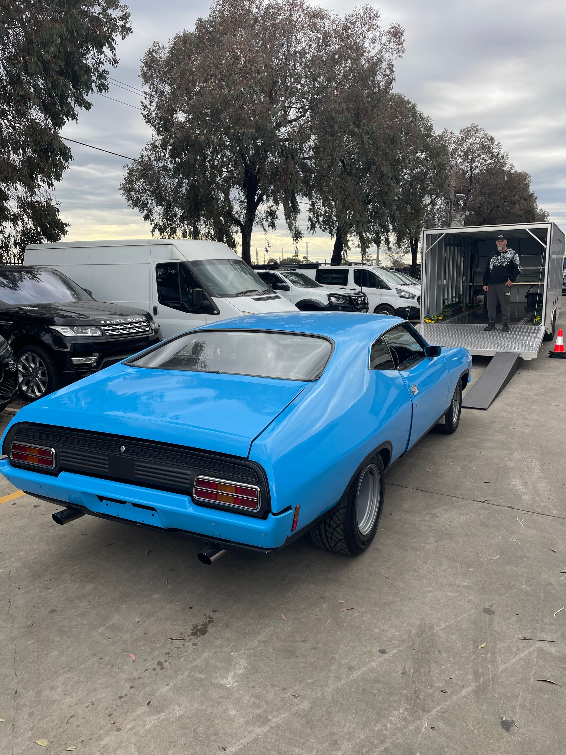 Bright blue classic muscle car parked at an outdoor auto show with trees and trailers nearby Full Throttle Enclosed Car Transport in Kilmore, VIC