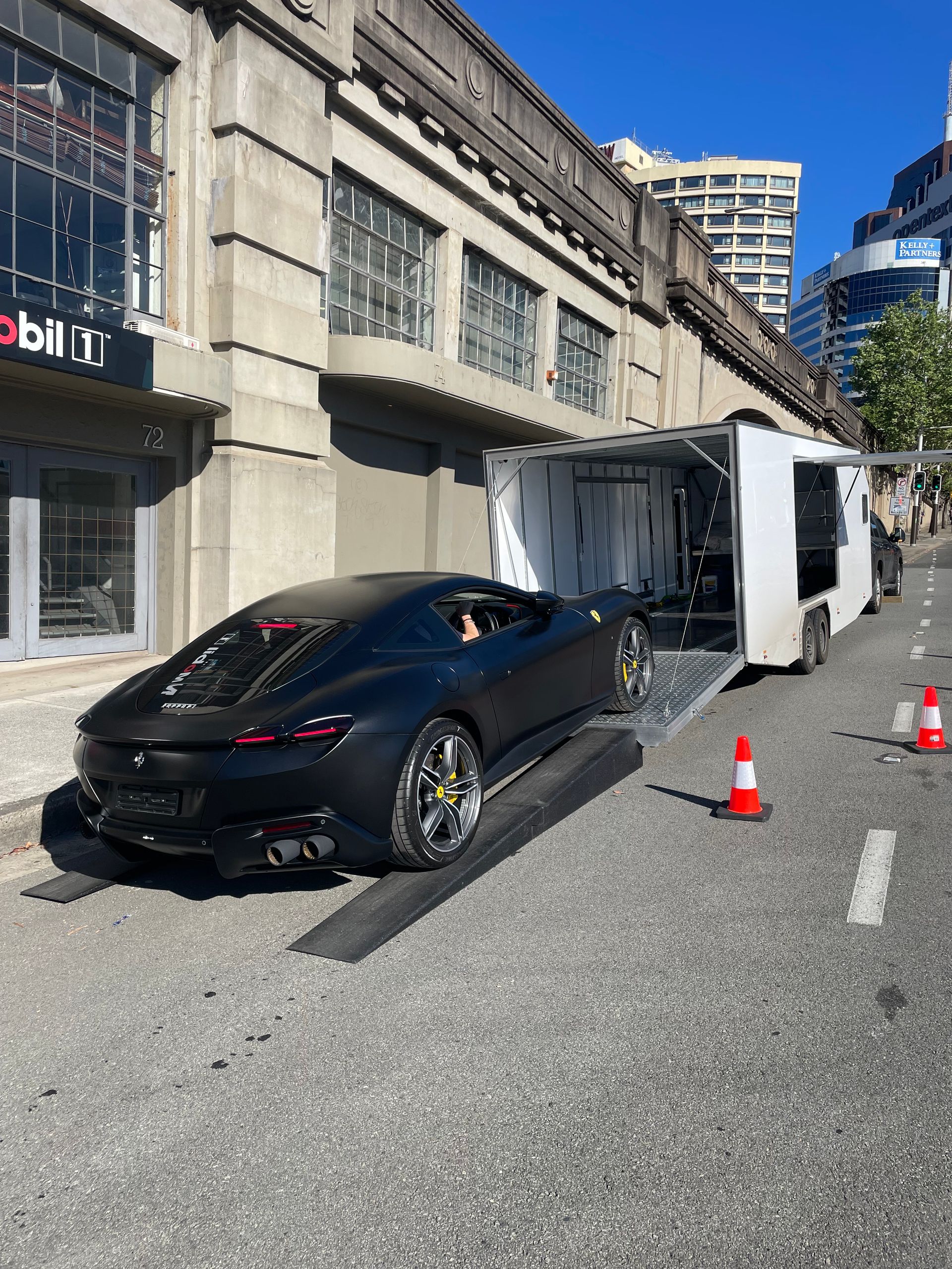 Black sports car being unloaded from a white trailer on a city street — Full Throttle Enclosed Car Transport in Kilmore, VIC