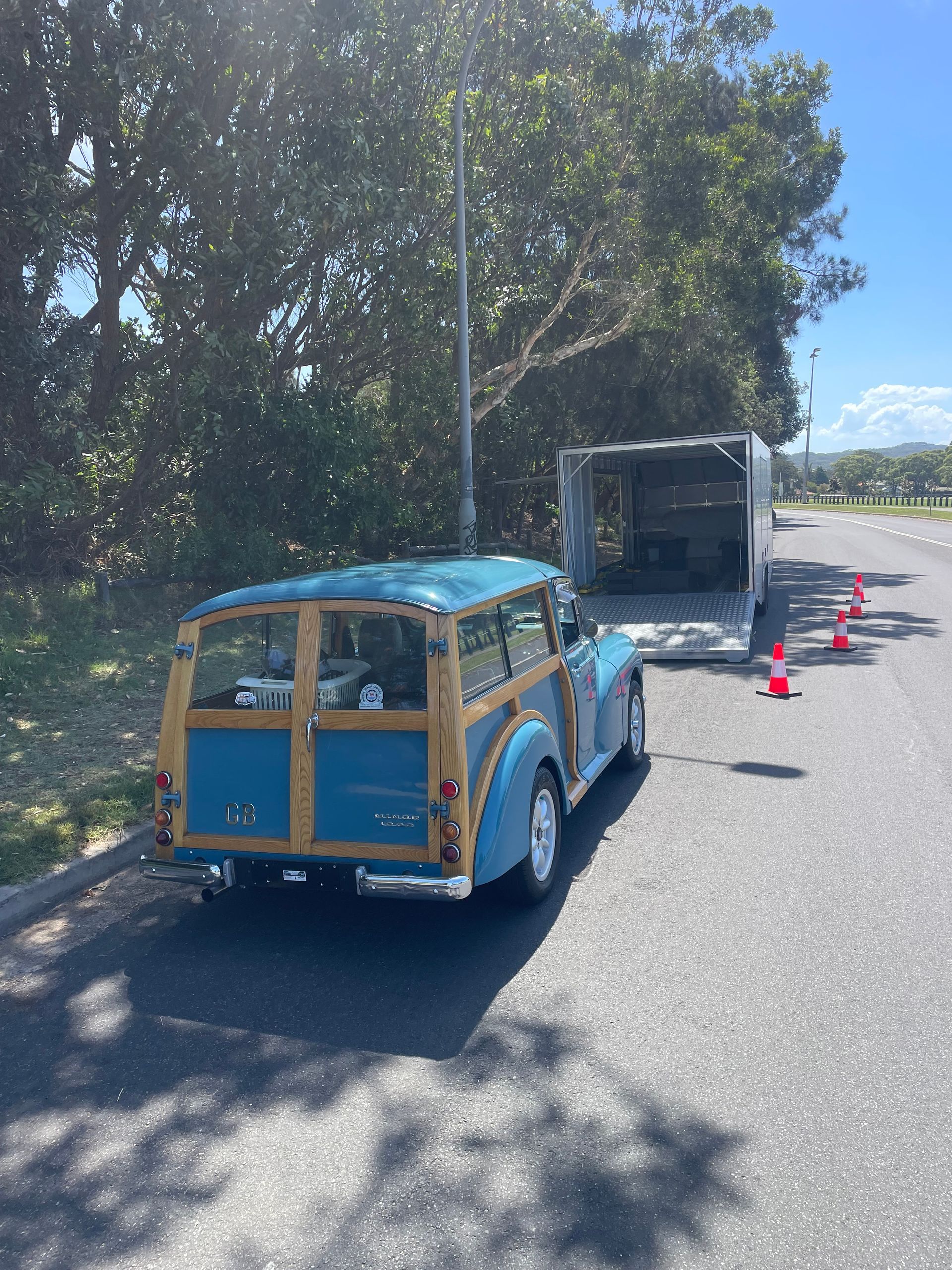 Blue and yellow toy truck towing a gray dumpster along a sunlit road - Full Throttle Enclosed Car Transport in Kilmore, VIC