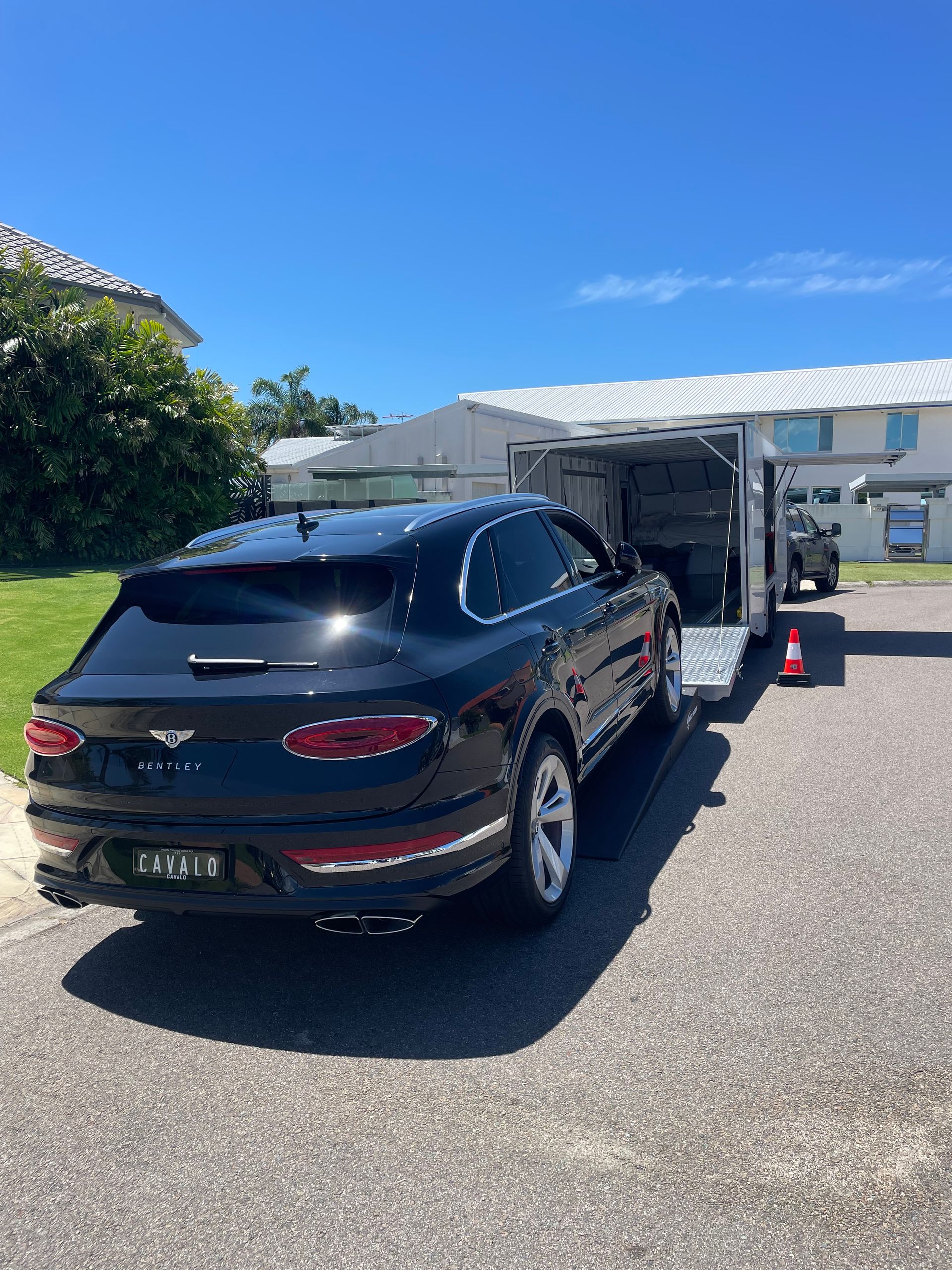 Black SUV hitched to a white enclosed trailer in a sunny driveway outside a house. - Full Throttle Enclosed Car Transport in Kilmore, VIC