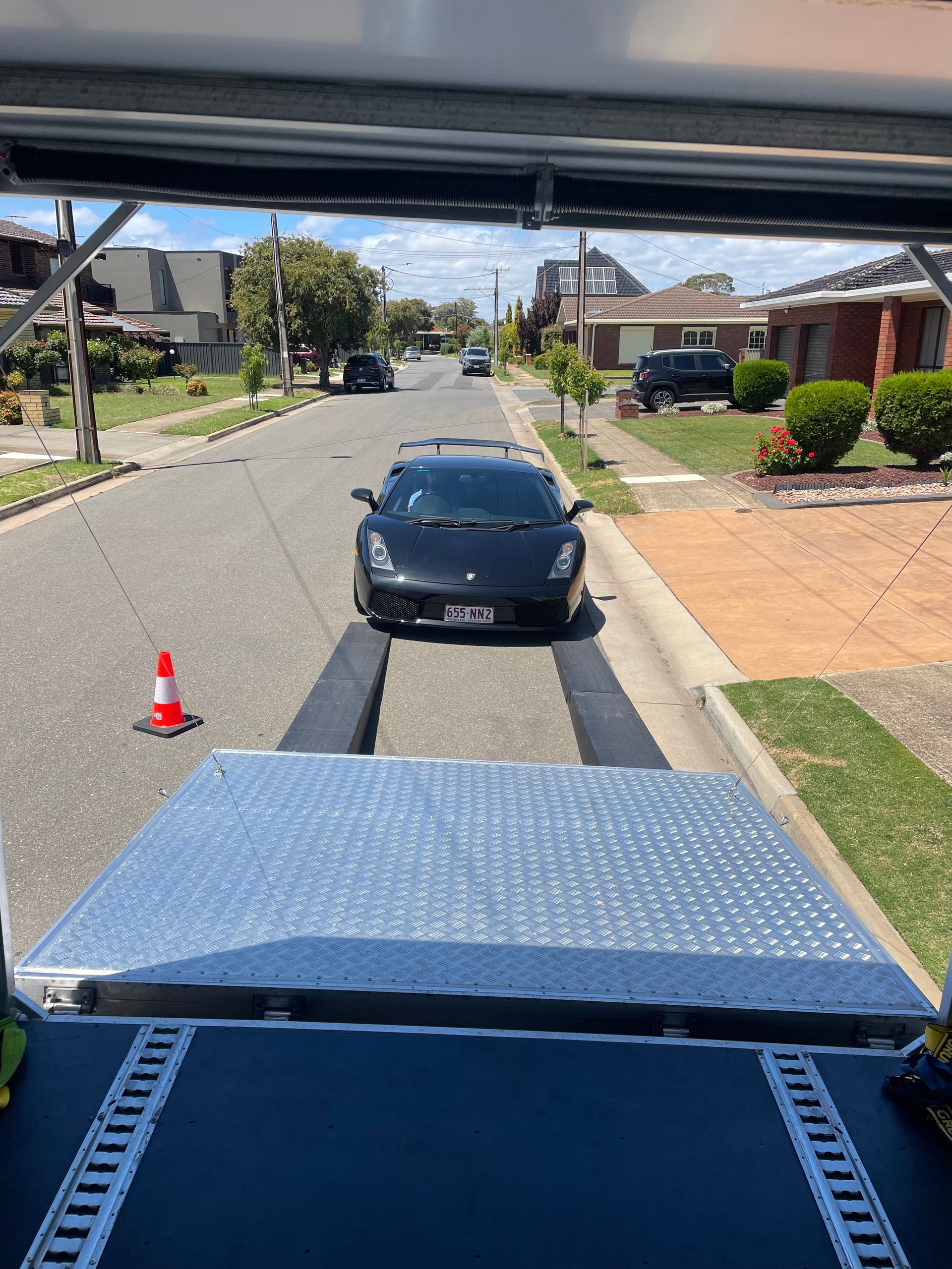 Tow truck view of a black car stopped behind a cone on a suburban street - Full Throttle Enclosed Car Transport in Kilmore, VIC