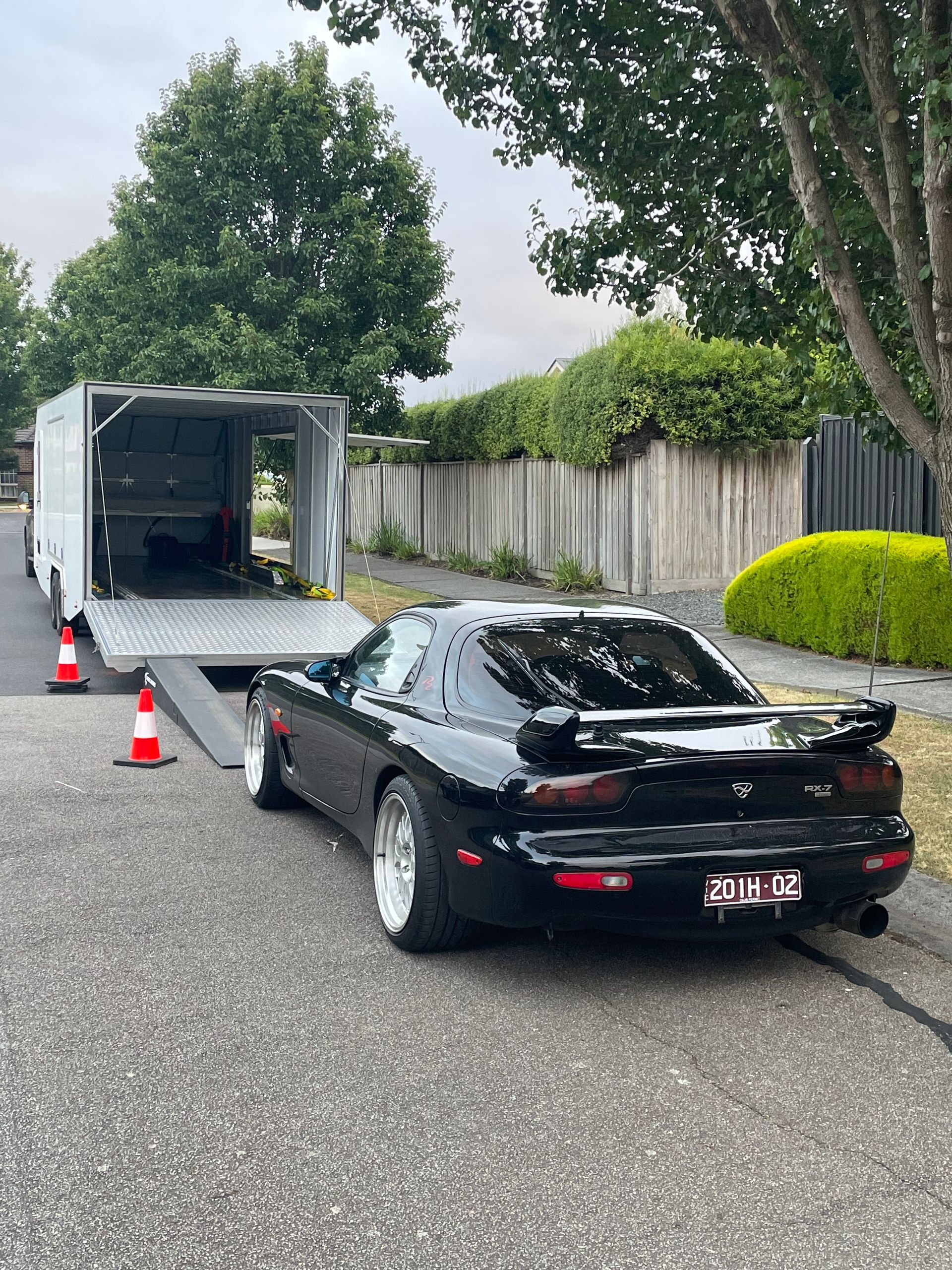 Black sports car behind an open white trailer on a street with traffic cones. - Full Throttle Enclosed Car Transport in Kilmore, VIC
