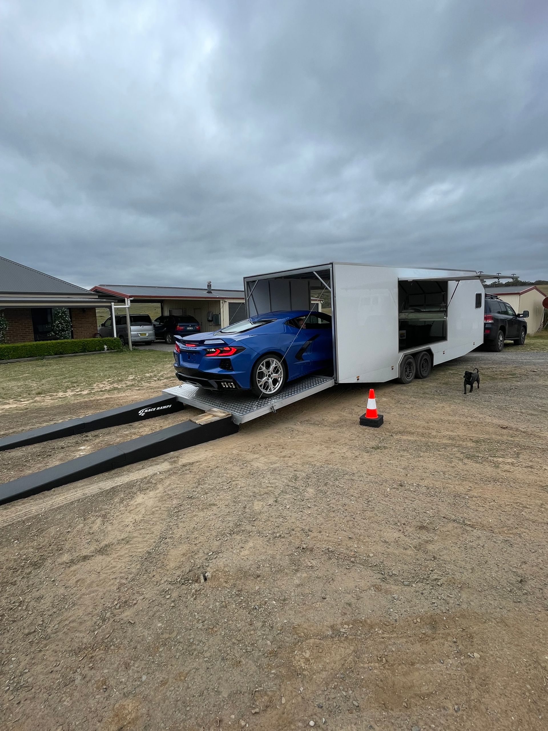 Blue car inside overturned white trailer on gravel road, with traffic cone under cloudy sky - Full Throttle Enclosed Car Transport in Kilmore, VIC