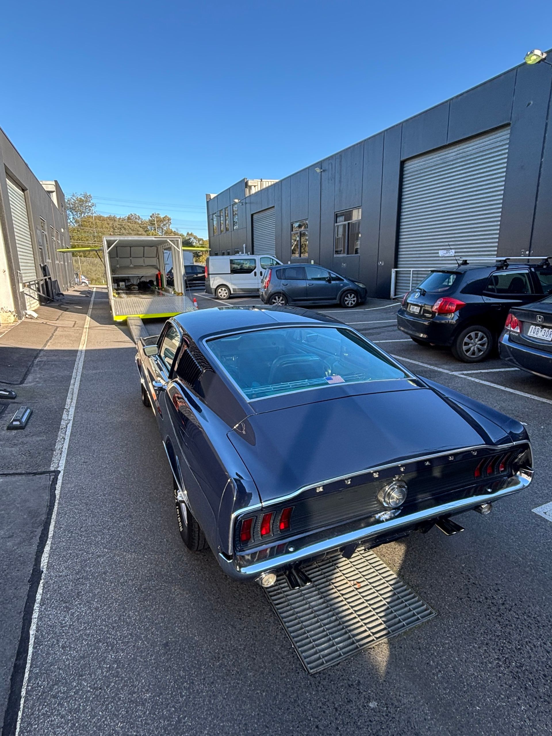 Dark blue vintage car parked in an industrial alley beside a warehouse and other parked vehicles - Full Throttle Enclosed Car Transport in Kilmore, VIC
