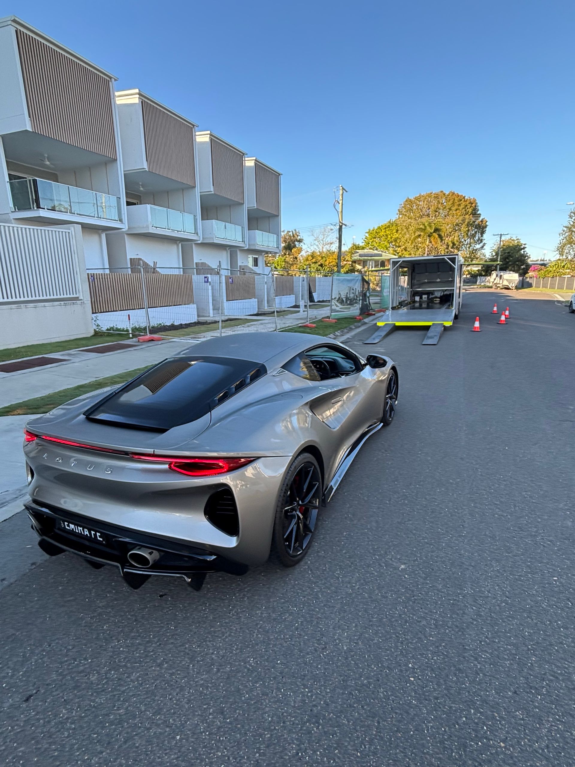 Silver sports car parked on a street beside a modern building with striped awnings and a truck ahead. - Full Throttle Enclosed Car Transport in Kilmore, VIC