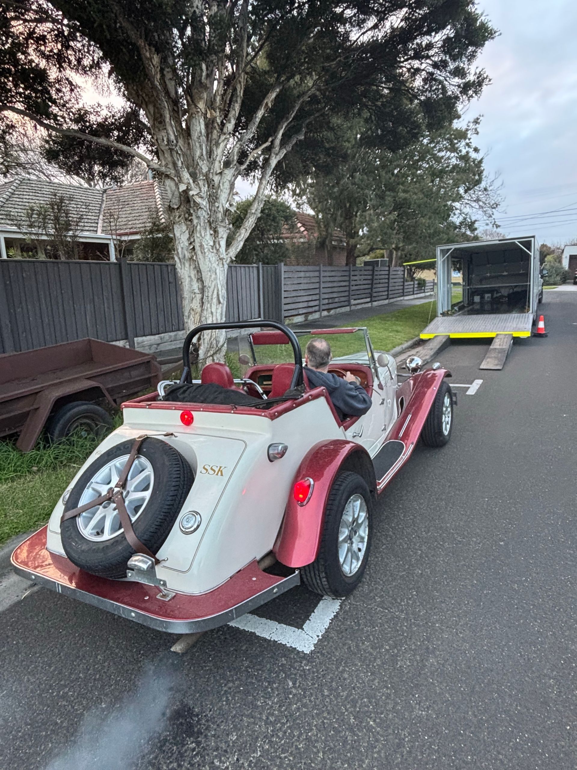 Red-and-white sports car on a flatbed trailer parked by a tree-lined street. - Full Throttle Enclosed Car Transport in Kilmore, VIC