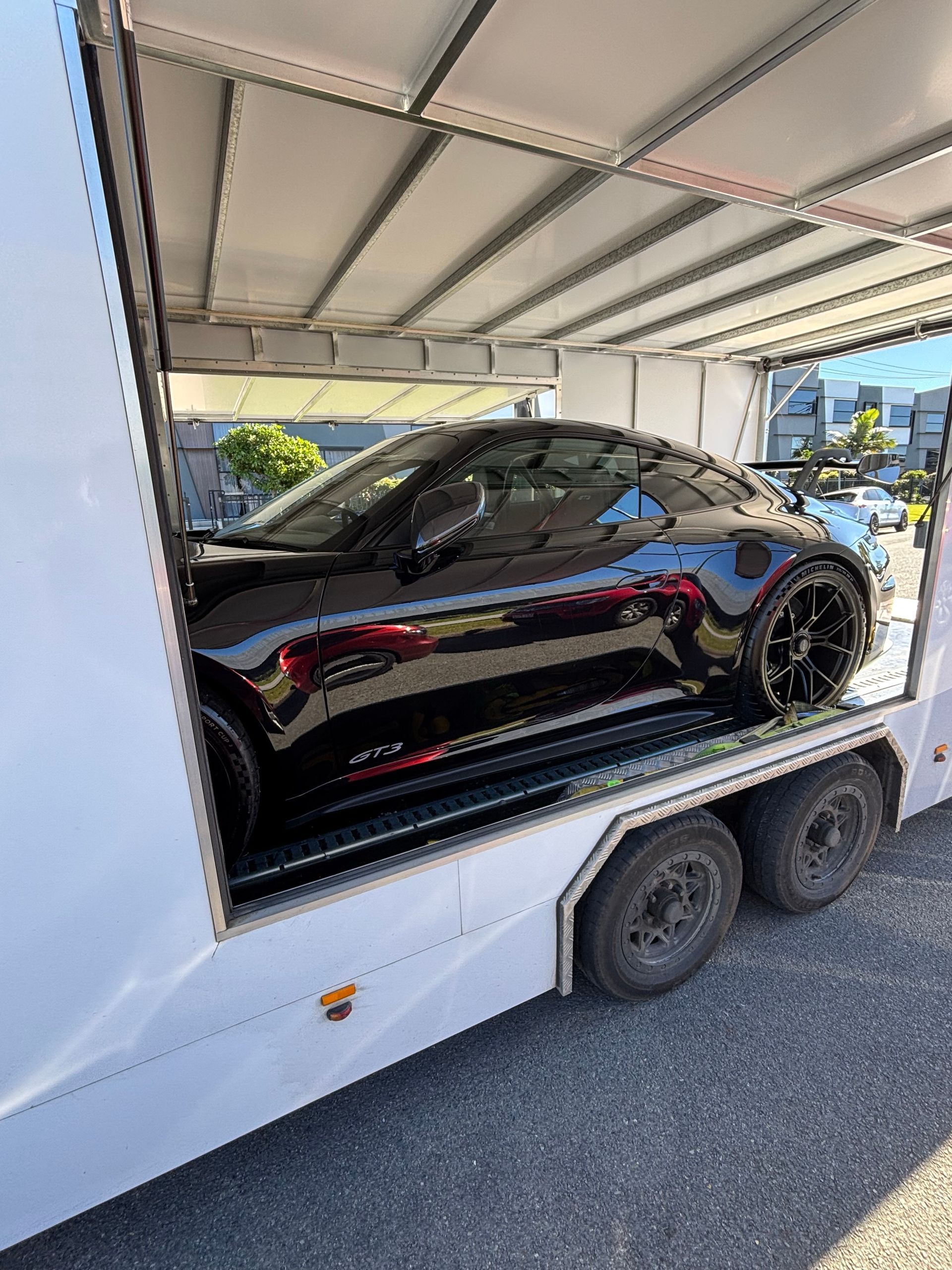 Black sports car secured inside a white enclosed trailer on a road. - Full Throttle Enclosed Car Transport in Kilmore, VIC