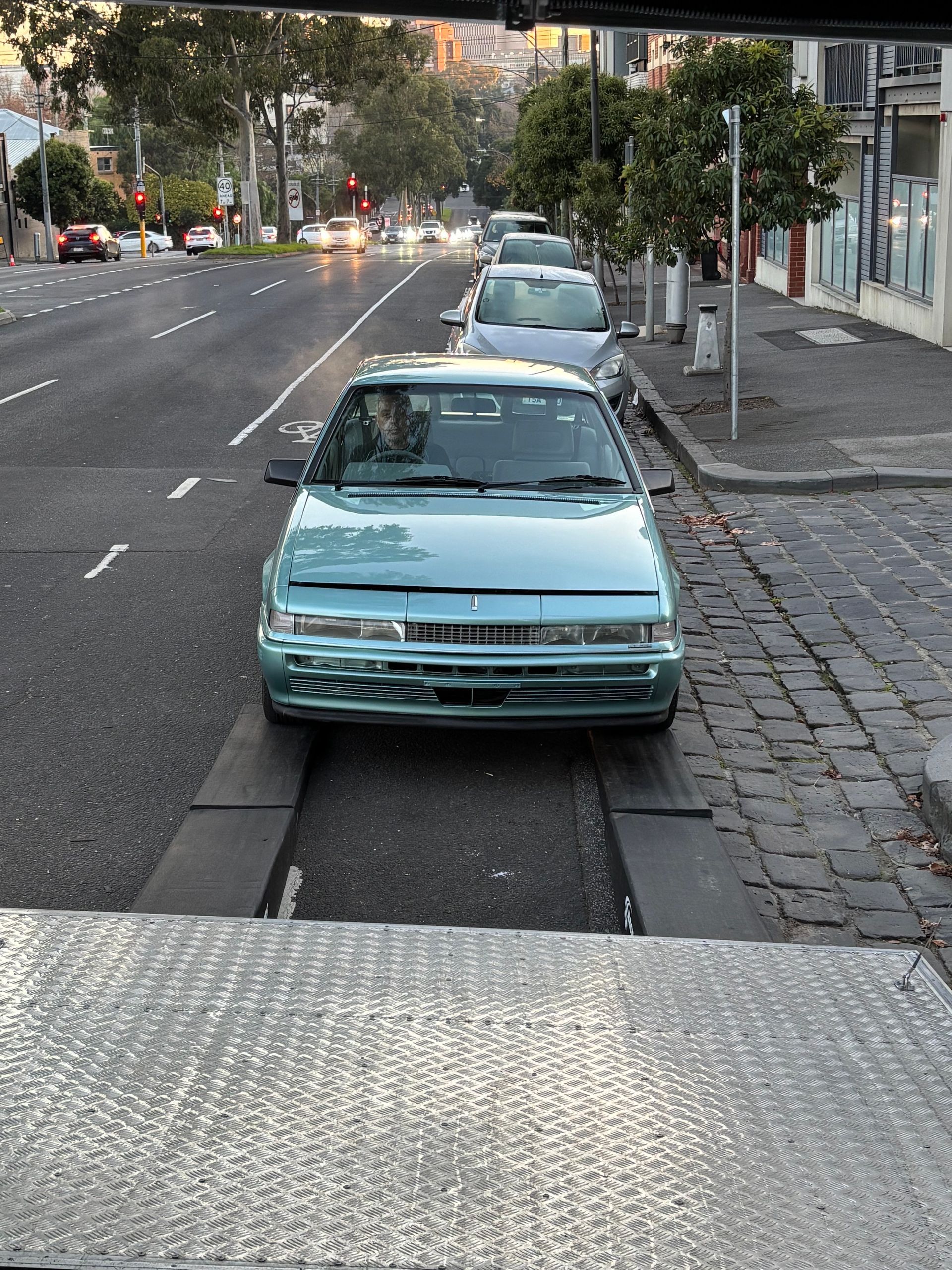 Teal car parked along a cobblestone curb on a city street at dusk - Full Throttle Enclosed Car Transport in Kilmore, VIC