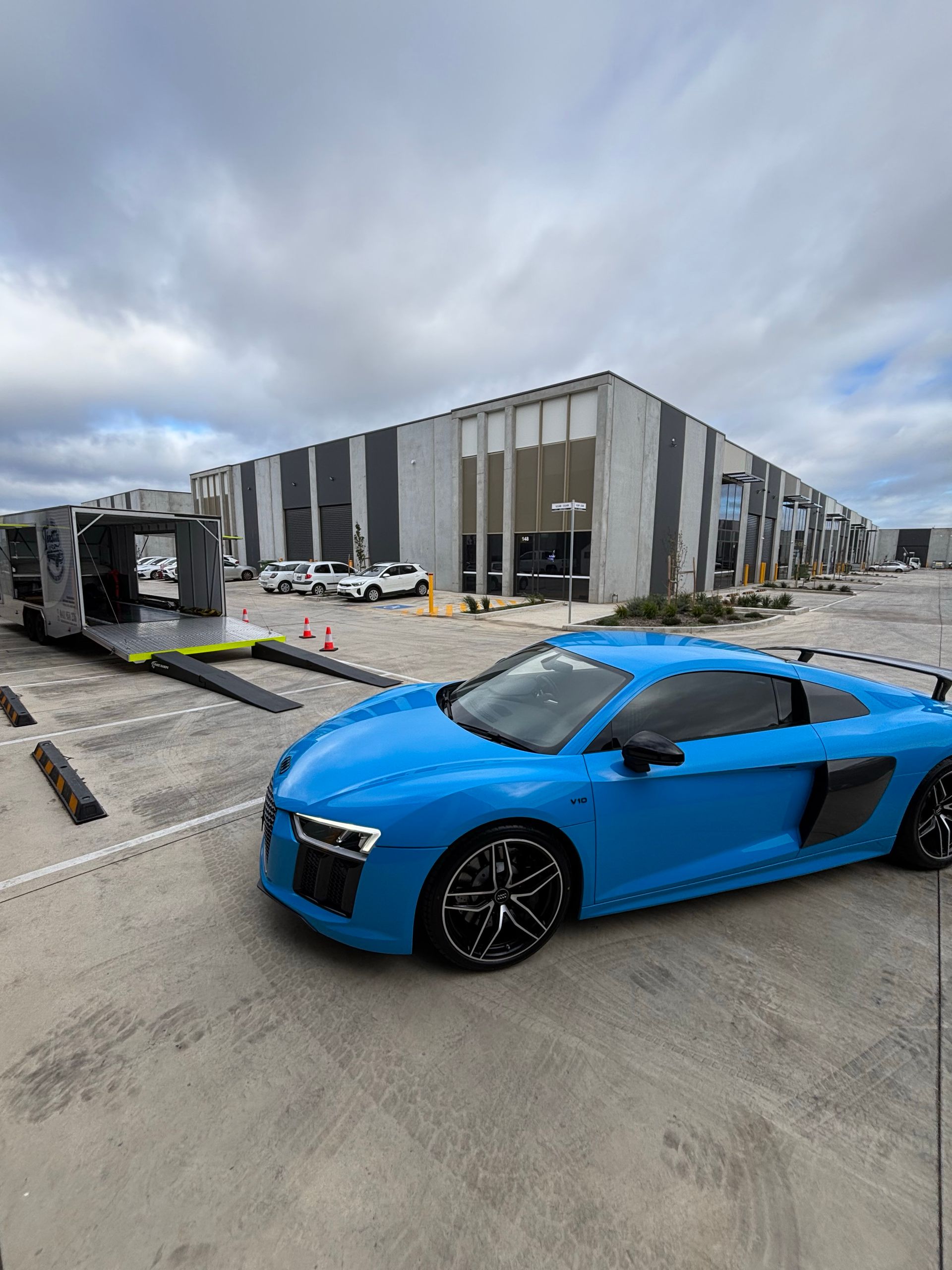 Bright blue sports car parked outside an industrial building on a concrete lot - Full Throttle Enclosed Car Transport in Kilmore, VIC