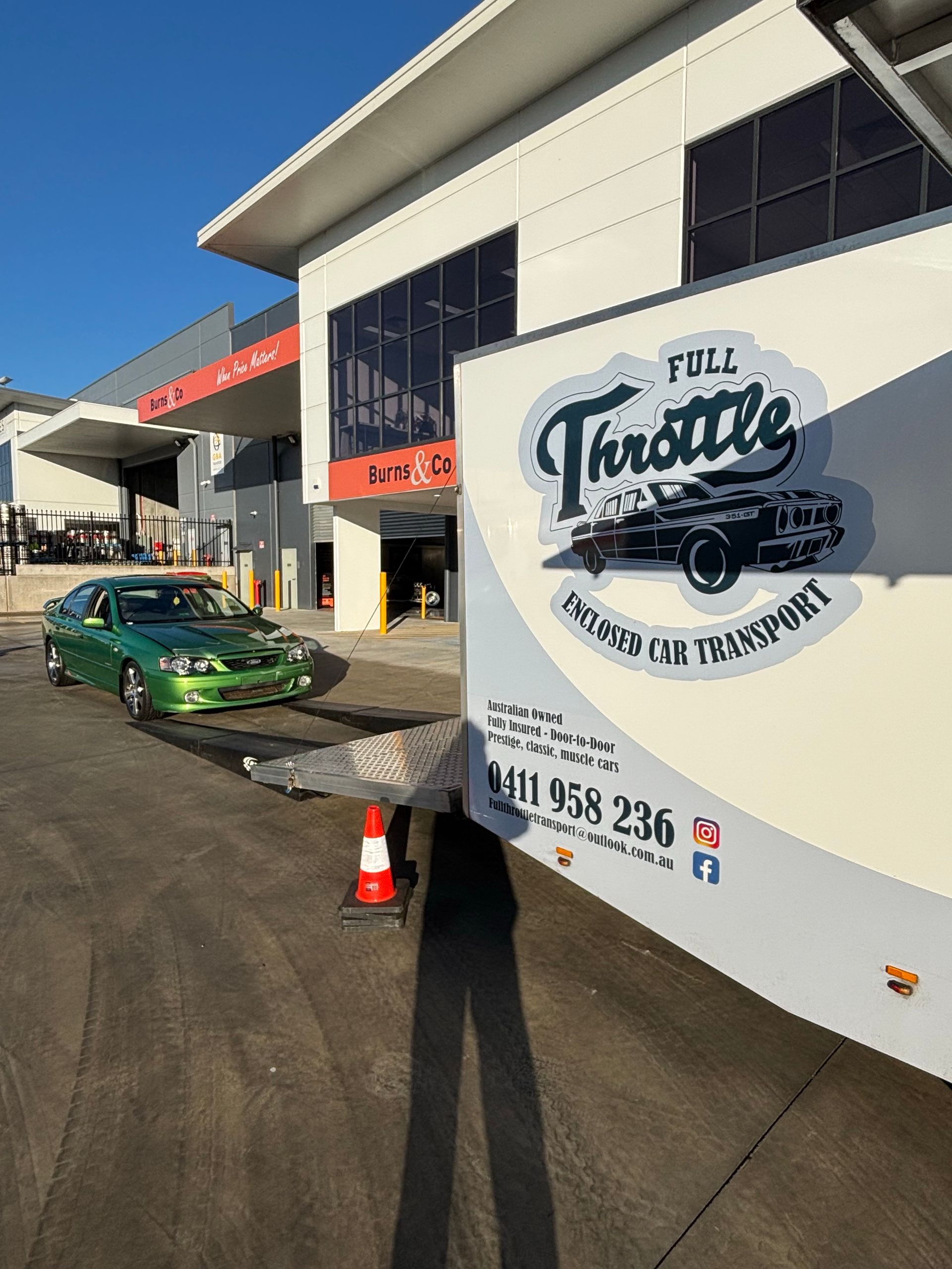 Food truck parked outside a white building, with a green car and orange cones nearby. - Full Throttle Enclosed Car Transport in Kilmore, VIC
