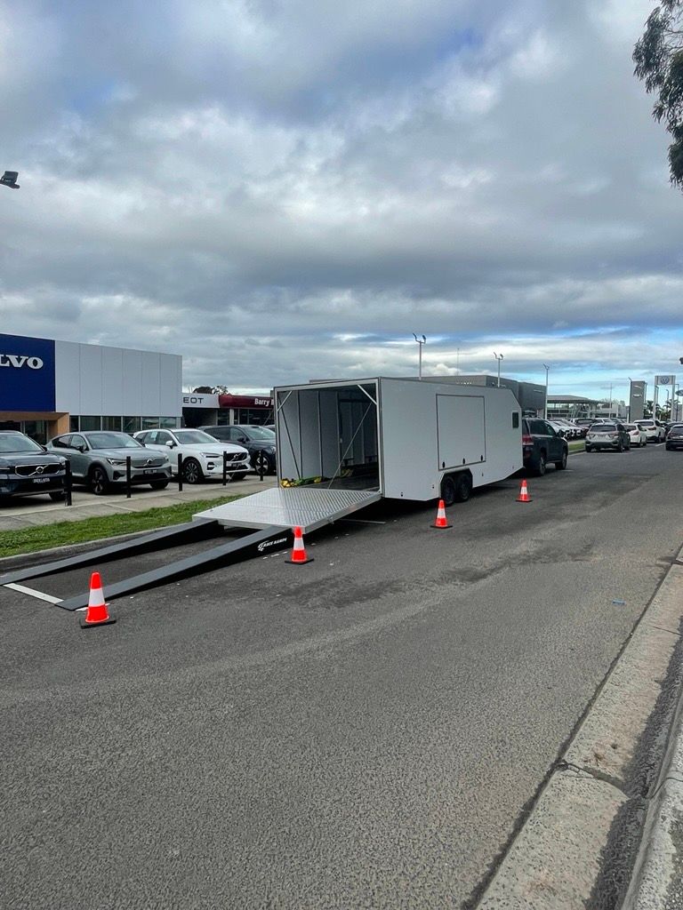 White enclosed trailer with ramp open on a road, parked near a car dealership — Full Throttle Enclosed Car Transport in Kilmore, VIC