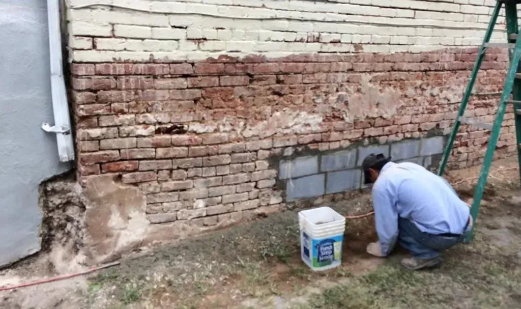 A man is kneeling down in front of a brick wall.