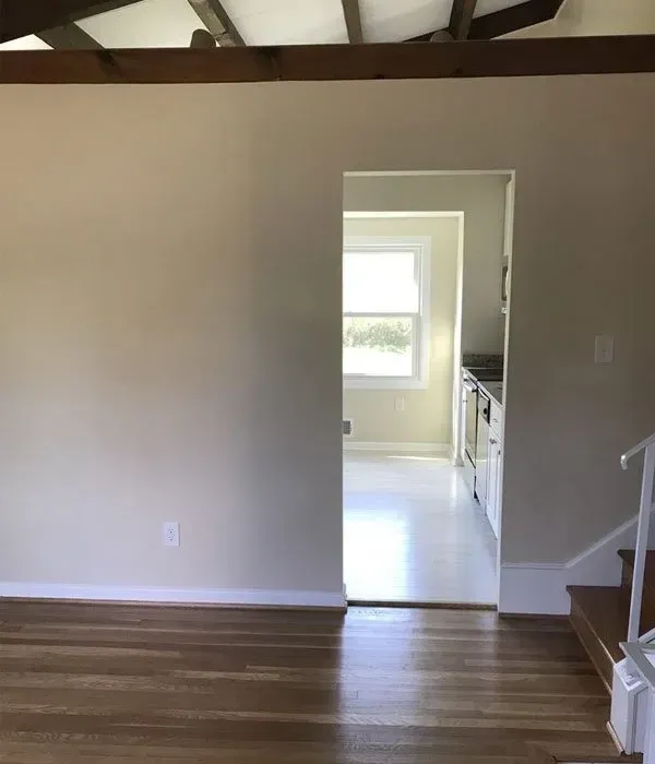 An empty room with hardwood floors and stairs leading to a kitchen.
