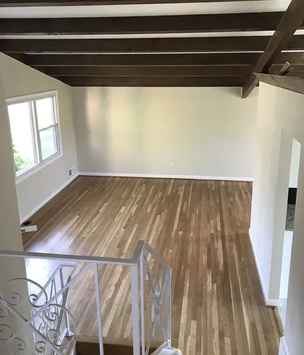 An empty living room with hardwood floors and a wooden ceiling.