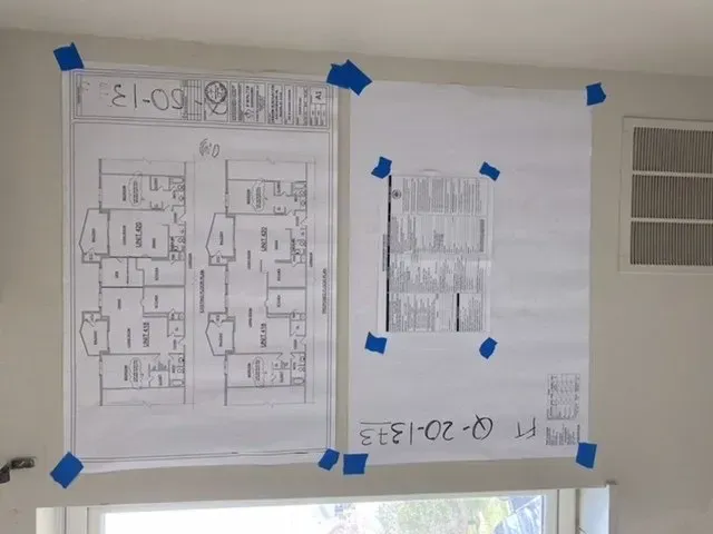 Two floor plans are taped to a wall and one of them says e1-00.