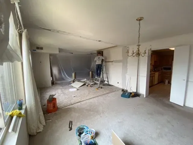A man is standing on a ladder in a living room.