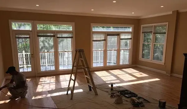 A man is kneeling in a living room with a ladder.