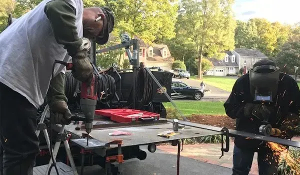 A man is using a drill while another man is welding a piece of metal.