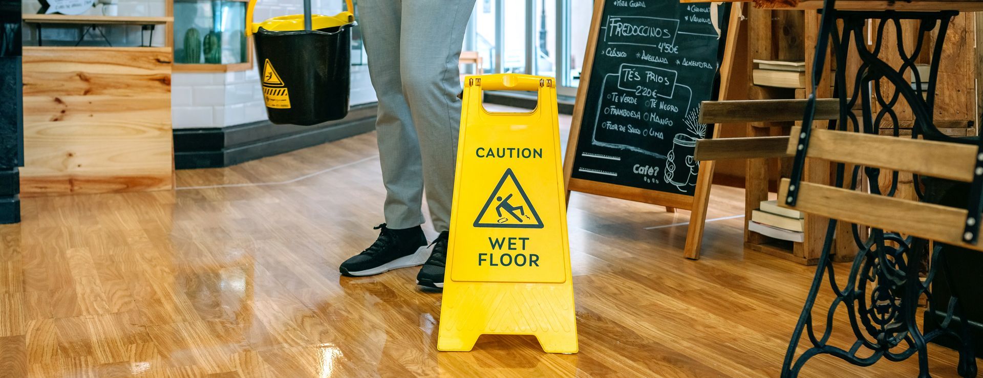 Person standing near wet floor sign in a cafe. Yellow sign with a triangle symbol.