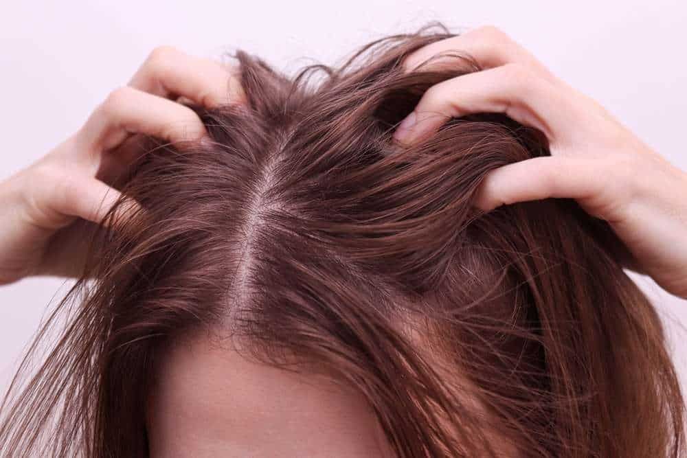 Hands parting a scalp with thinning hair and visible roots