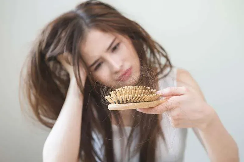 Woman holding a hairbrush and looking concerned at tangled hair on a light background