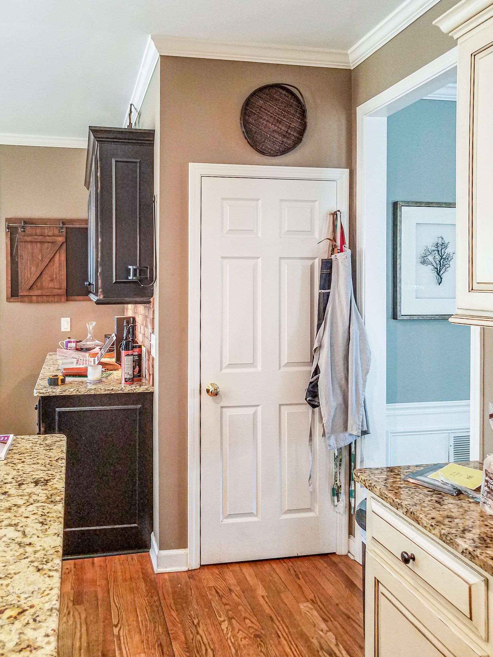 Kitchen with tan walls, white door, wood floors, and granite counters beside a bathroom doorway.