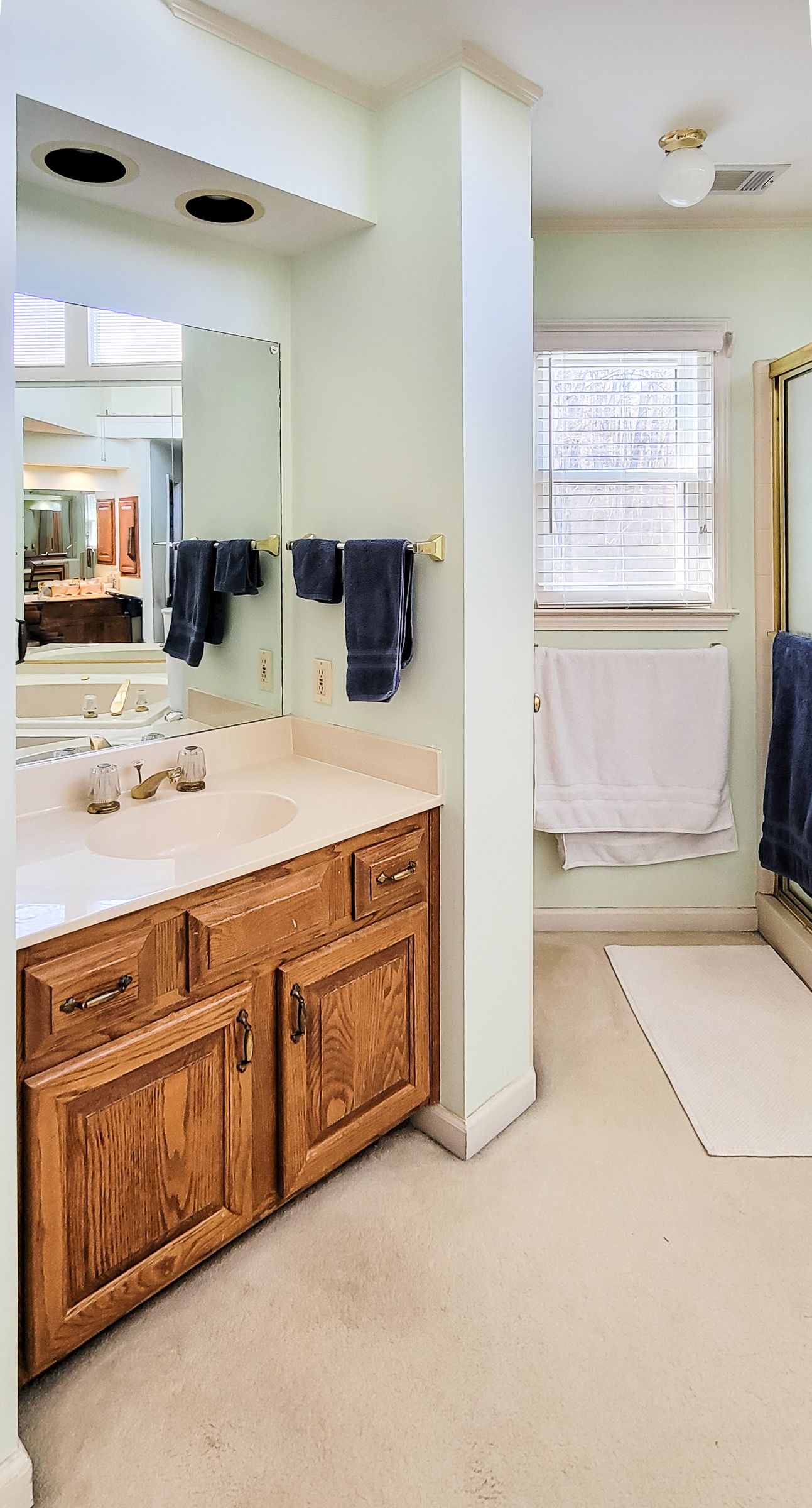Bright bathroom with double vanity, mirrors, towel rack, and window by a shower curtain.