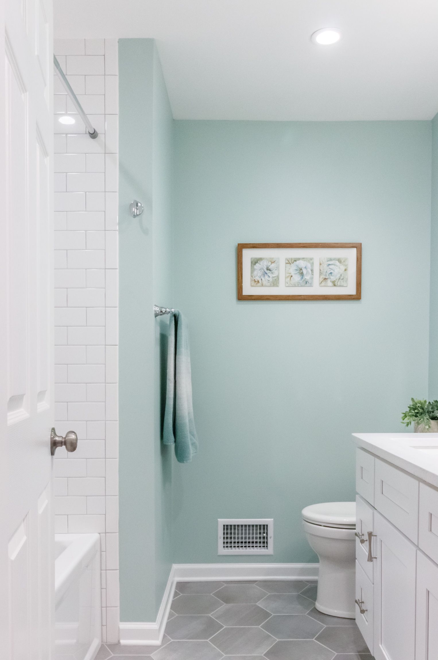 Bright bathroom with pale blue walls, white vanity, toilet, and tiled shower wall.