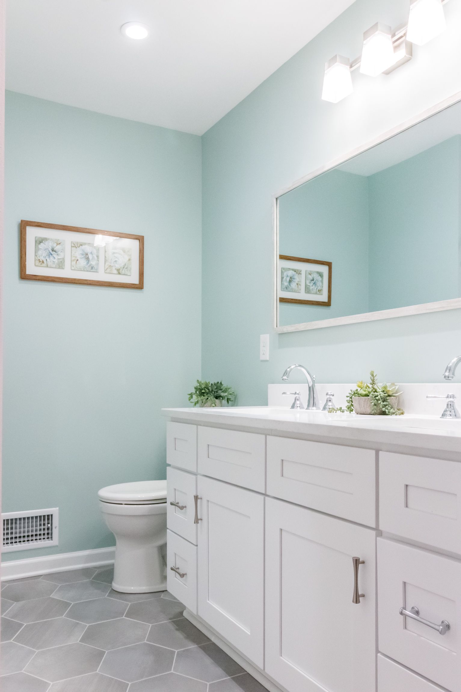 Bright bathroom with white vanity, large mirror, toilet, and light blue walls.