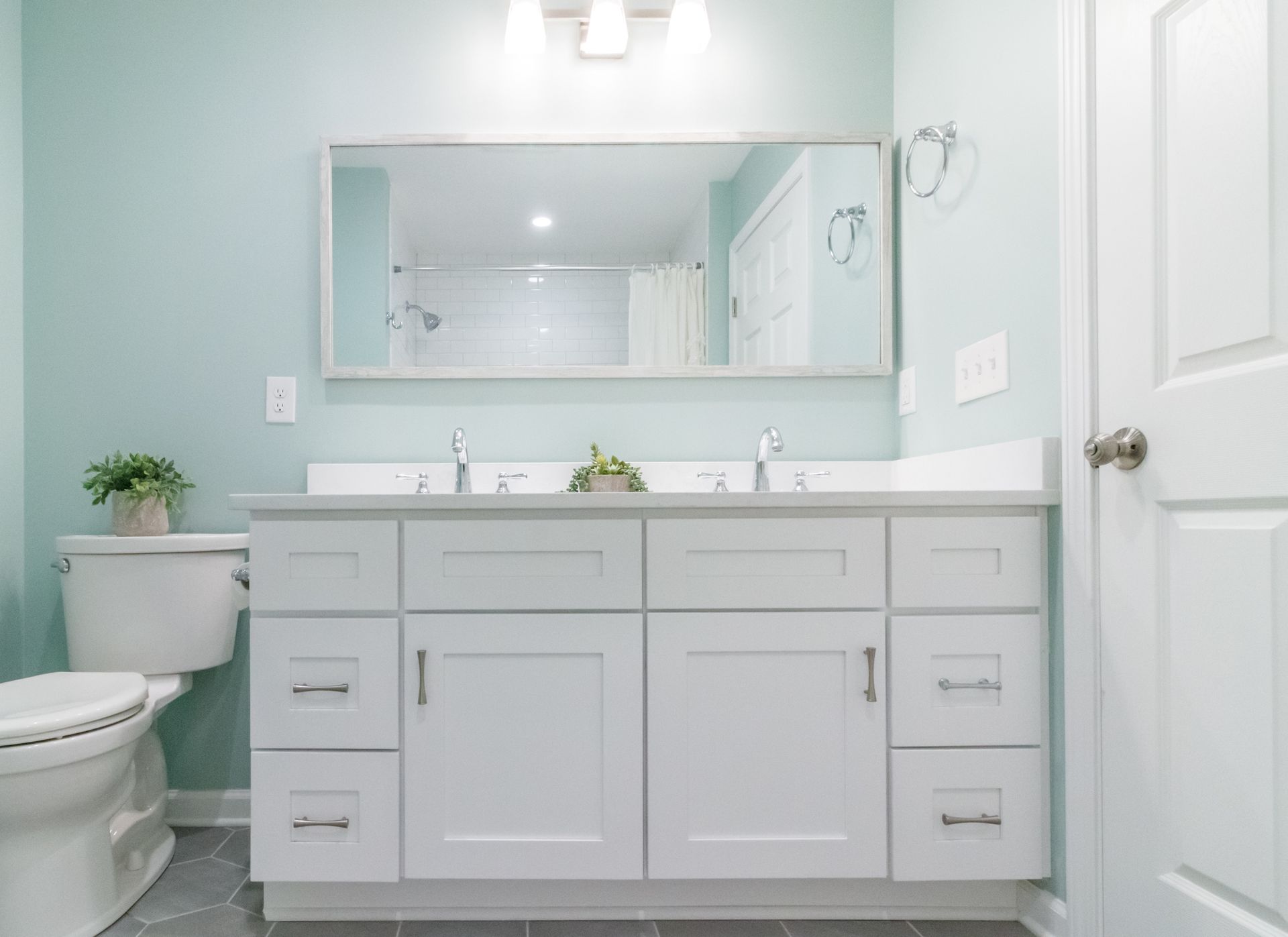 Light gray bathroom vanity with double sinks, large mirror, and toilet in a bright room
