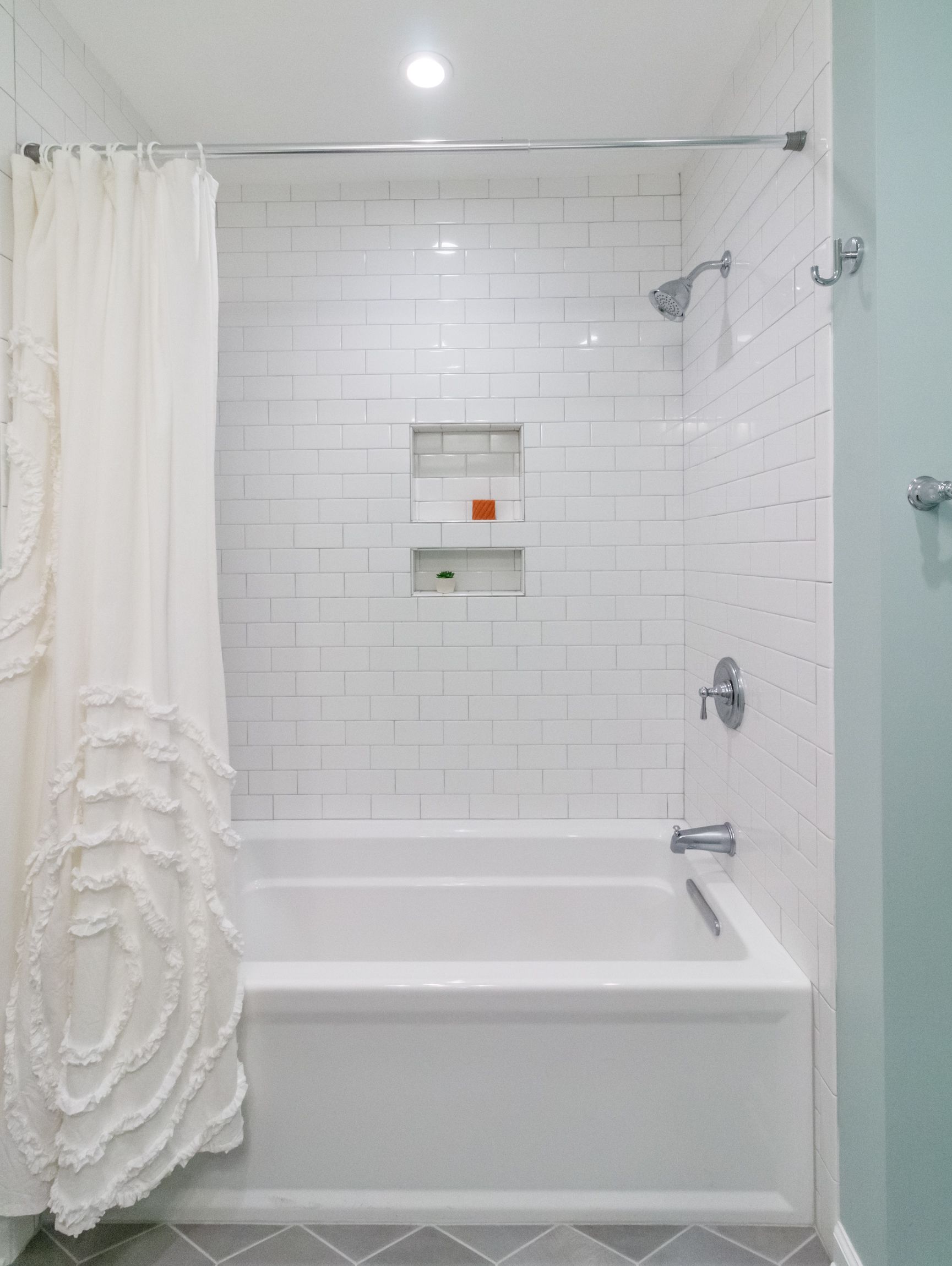 White tiled bathroom with a bathtub, shower curtain, and built-in shelf niche