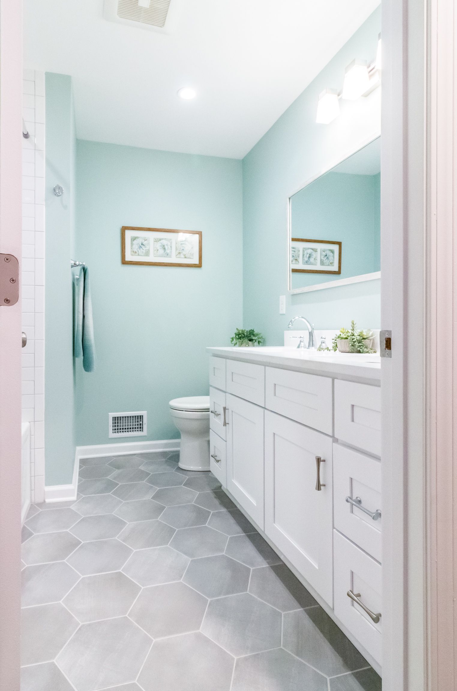 Bright mint-green bathroom with white vanity, mirror, toilet, and hexagon tile floor.
