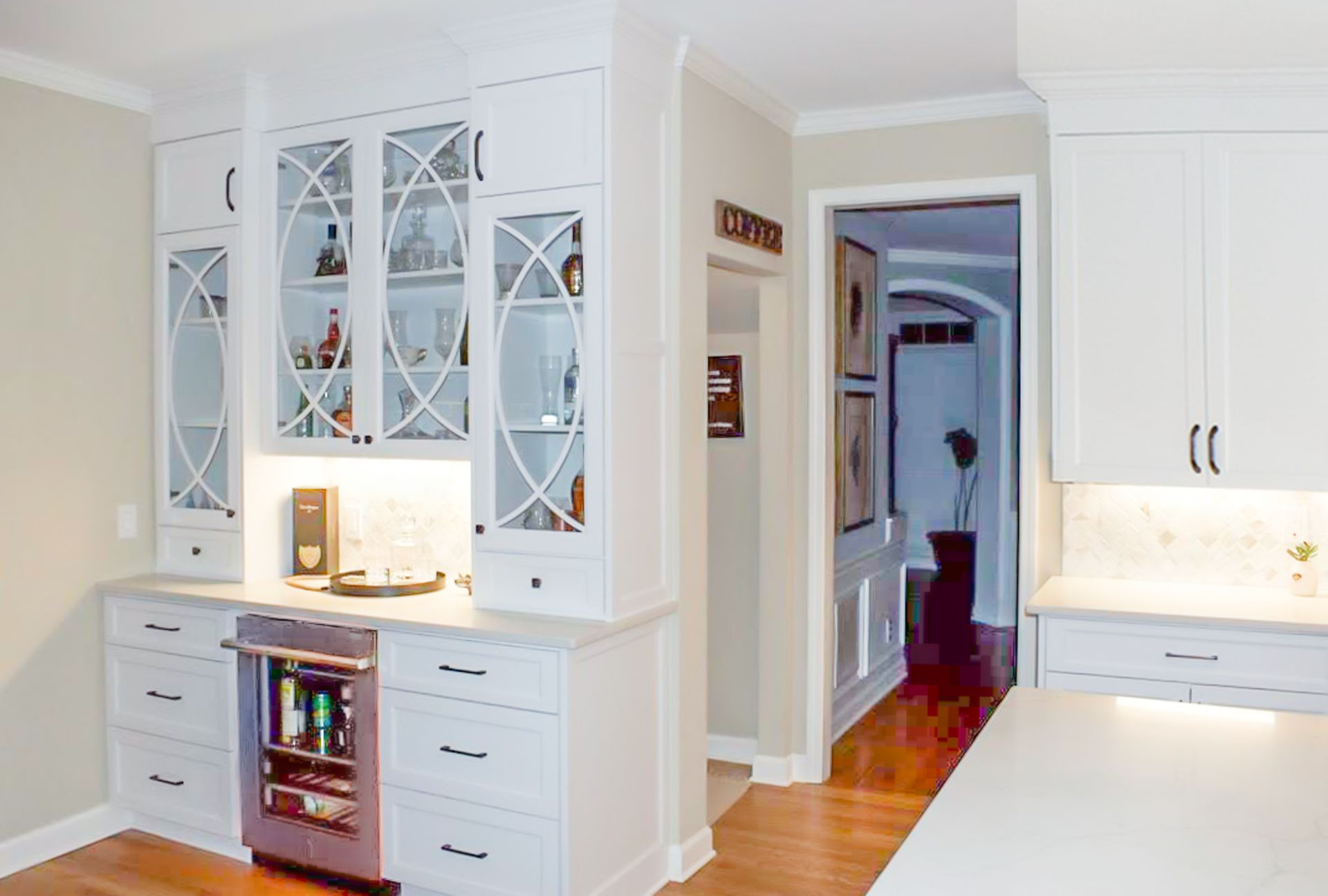 Bright white kitchen with glass-front cabinets, drawers, and a view into a hallway.