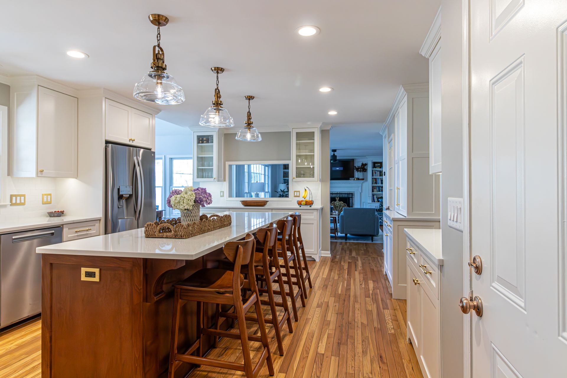 Bright modern kitchen with island, wooden bar stools, white cabinets, and hardwood floors