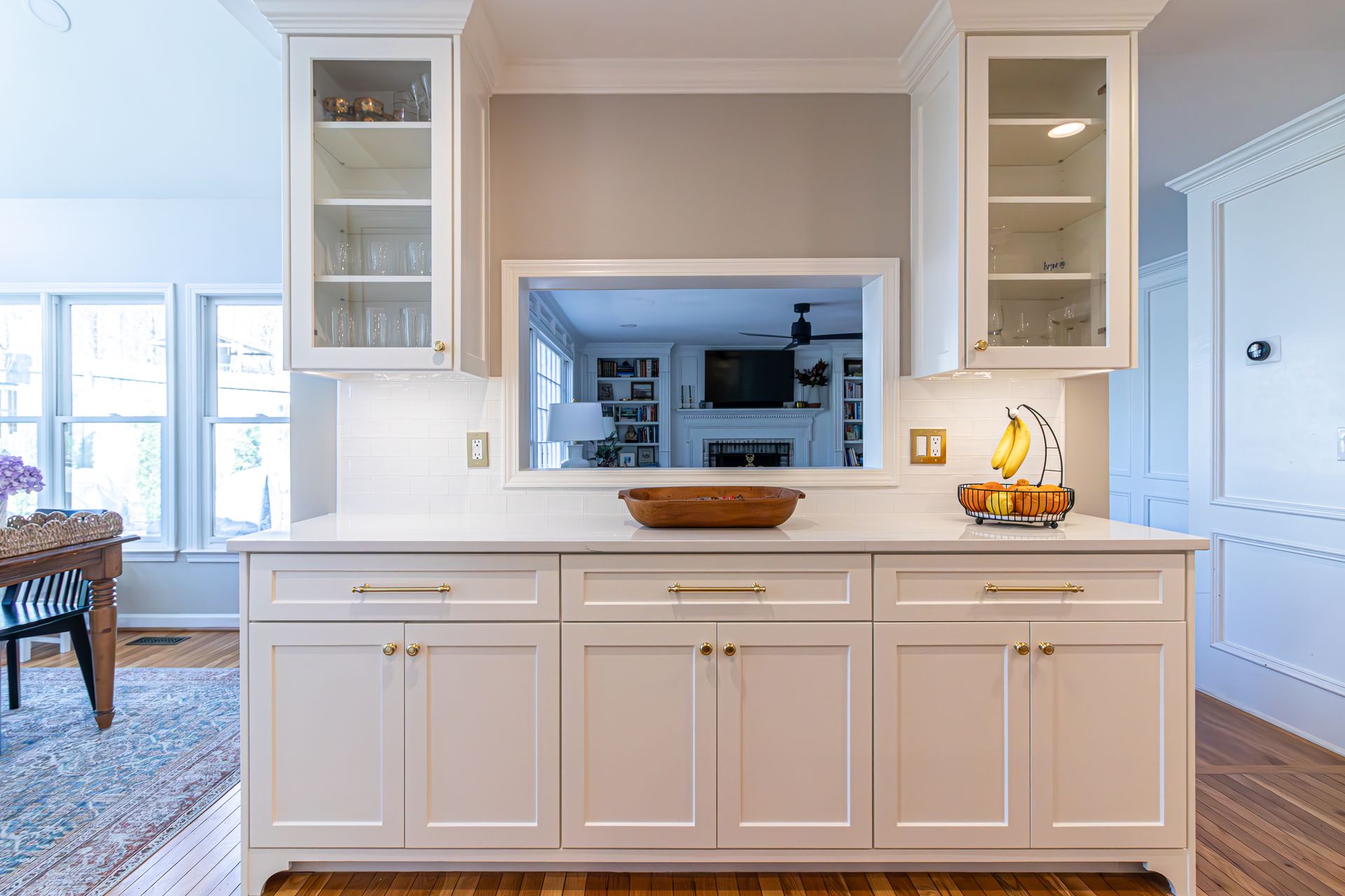 Bright kitchen island with built-in cabinets, framed by white shelves and a pass-through to a living room.