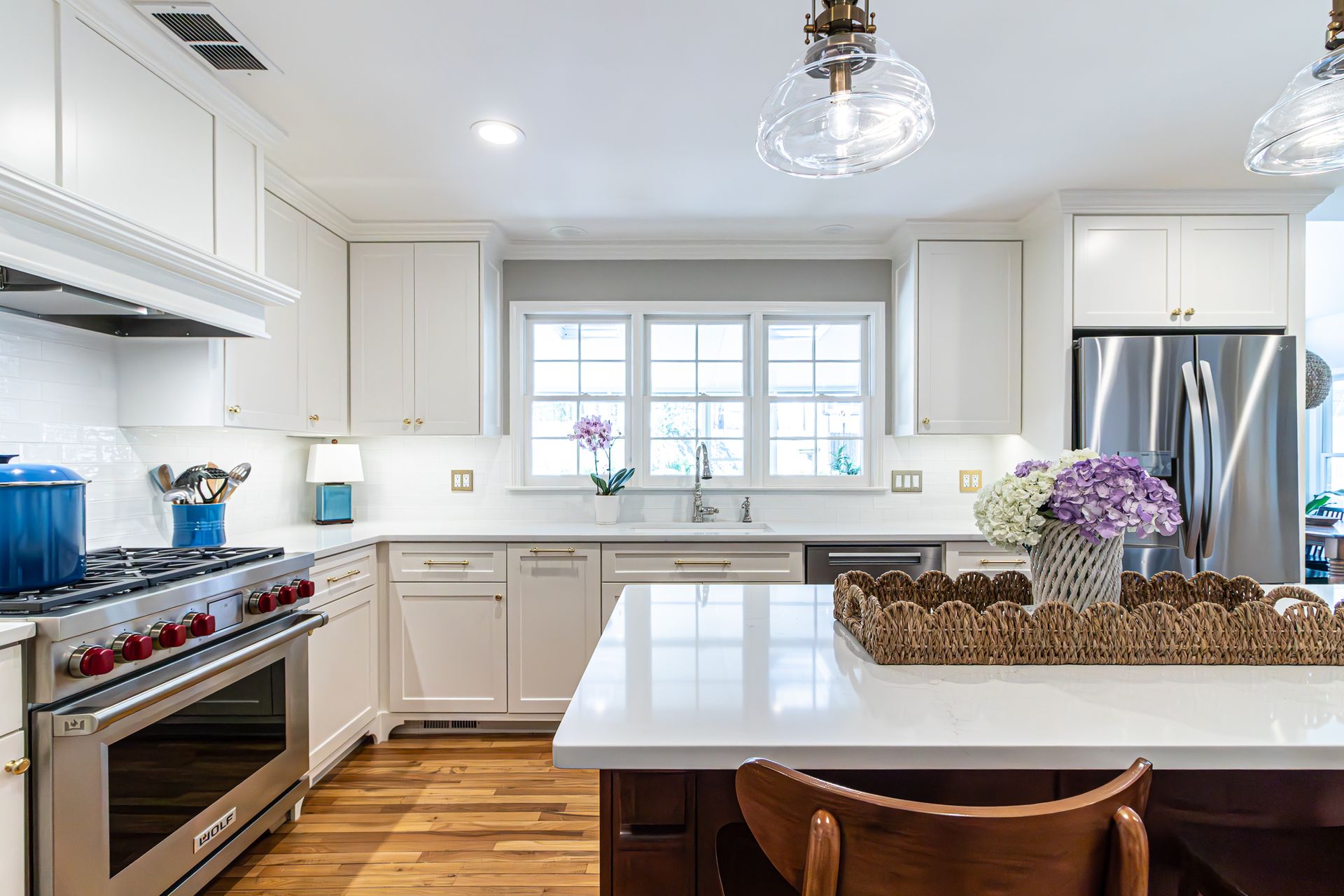 Bright white kitchen with stainless steel stove, island, and pendant lights, viewed from the center