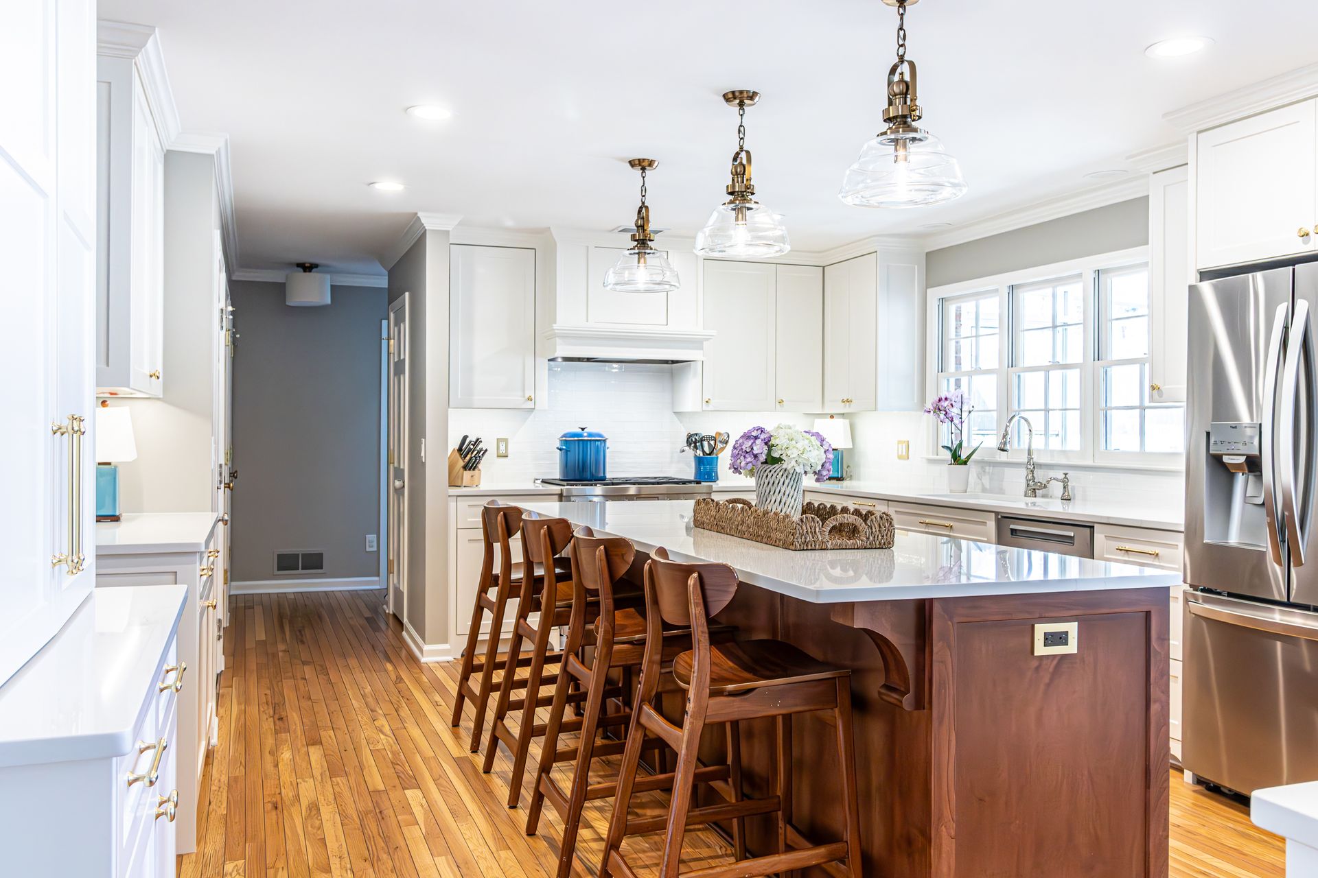 Bright kitchen with white cabinets, marble island, wooden stools, and stainless steel appliances.
