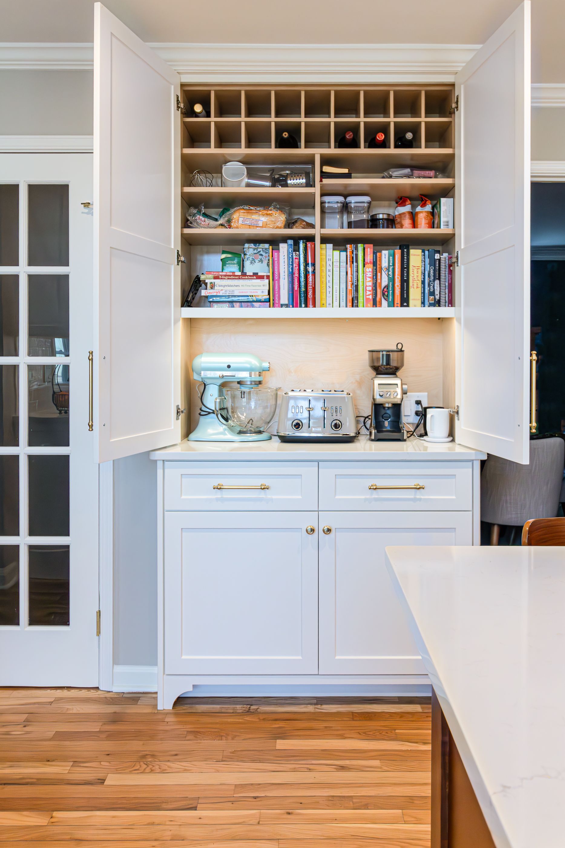 White kitchen cabinet with open shelves, dishes, small appliances, and books beneath warm under-cabinet lighting.
