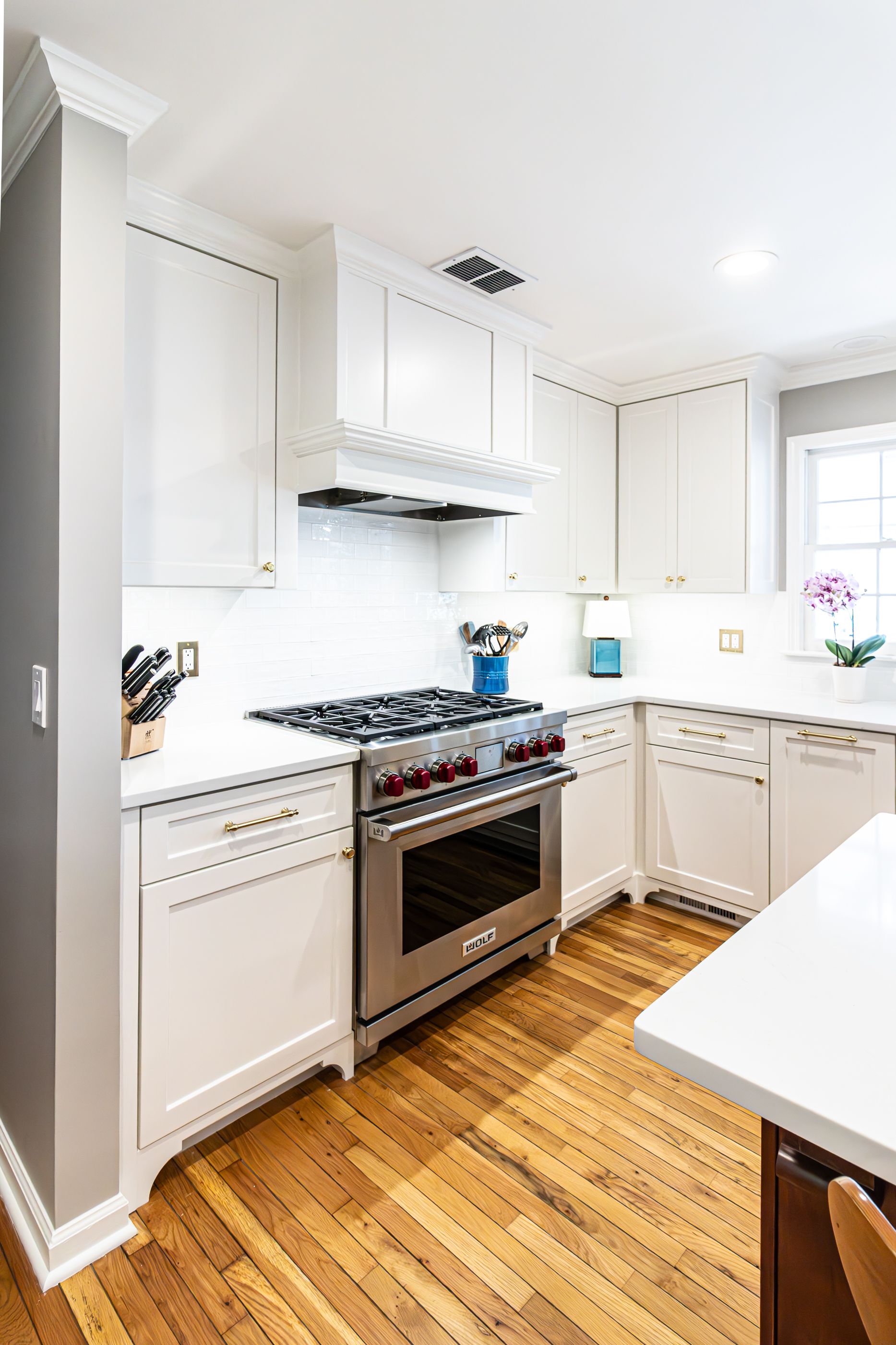Bright white kitchen with gas stove, wood floors, and sunlight from a window