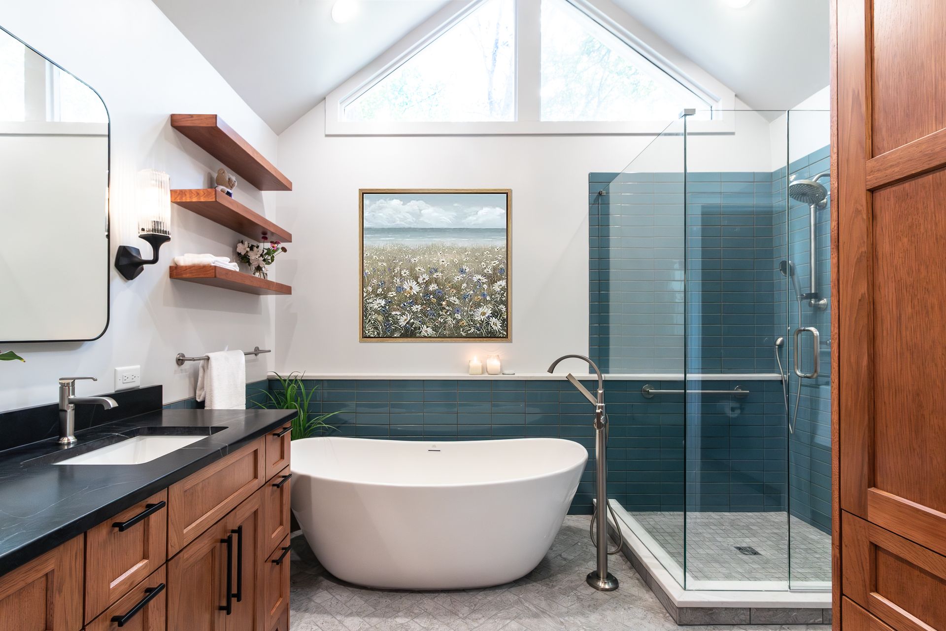 Modern bathroom with freestanding tub, glass shower, black vanity, and skylight under a vaulted ceiling