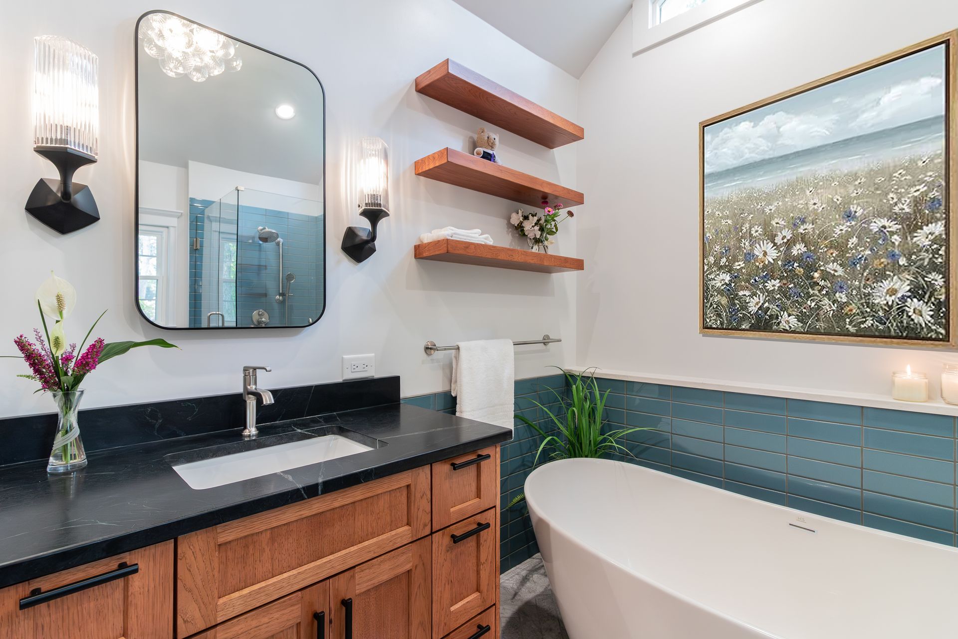 Modern bathroom with wood vanity, black countertop, freestanding tub, and floral wall art