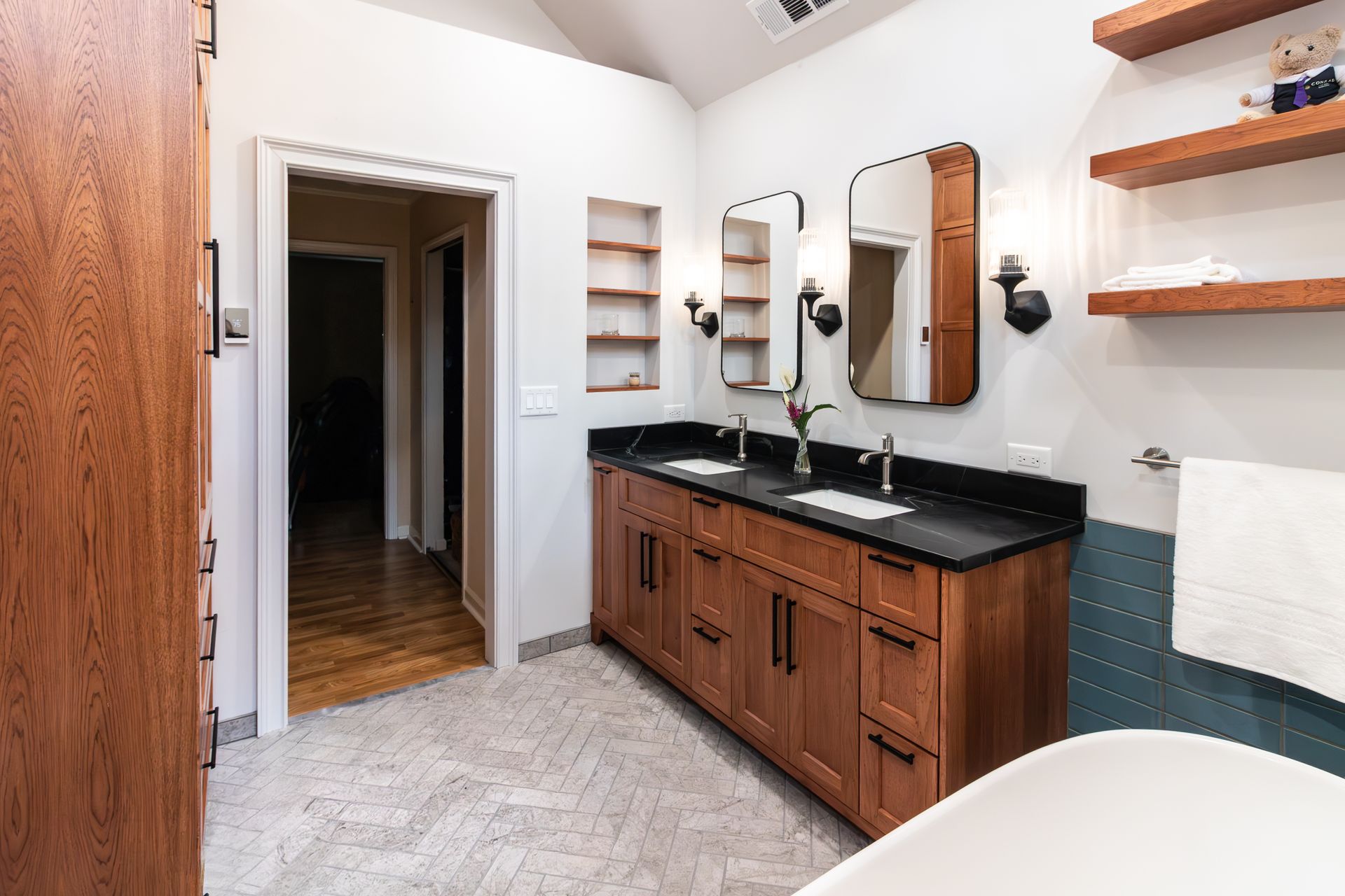 Modern bathroom with wooden vanity, black countertop, mirror, wall shelves, and white walls