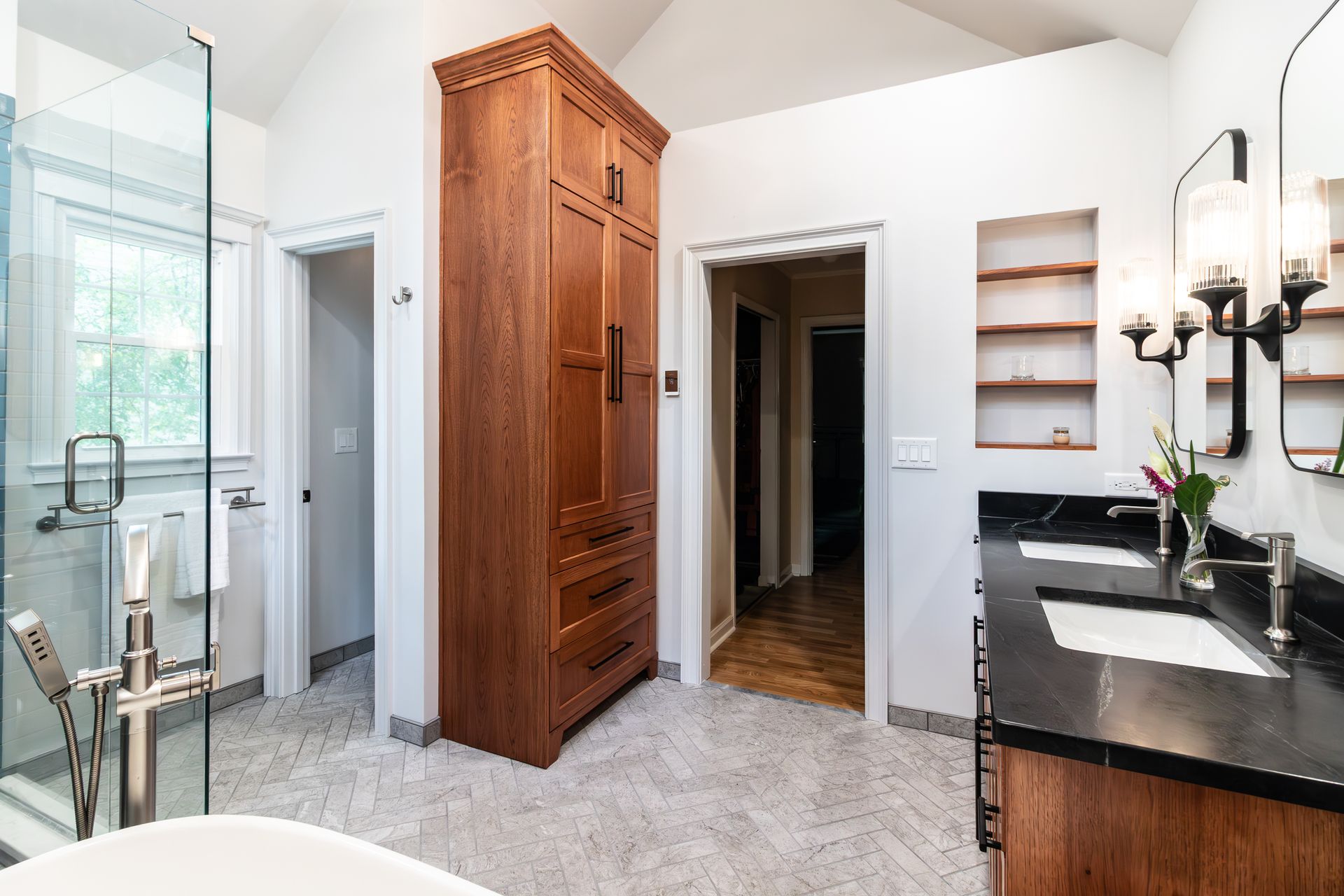 Modern bathroom with glass shower, tall wood cabinet, black countertop, and white tile floor